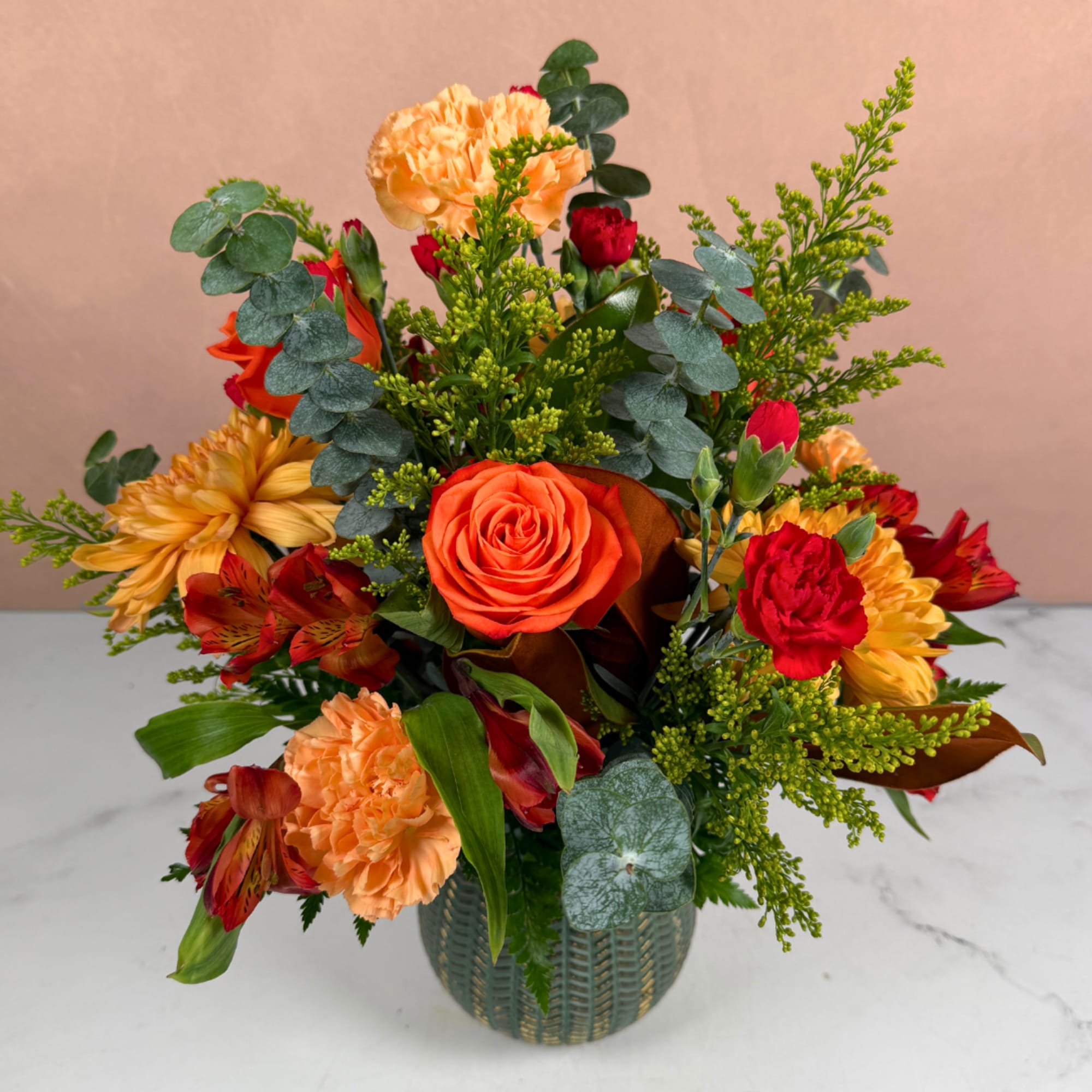 Orange and red mixed flower arrangement in a textured vase