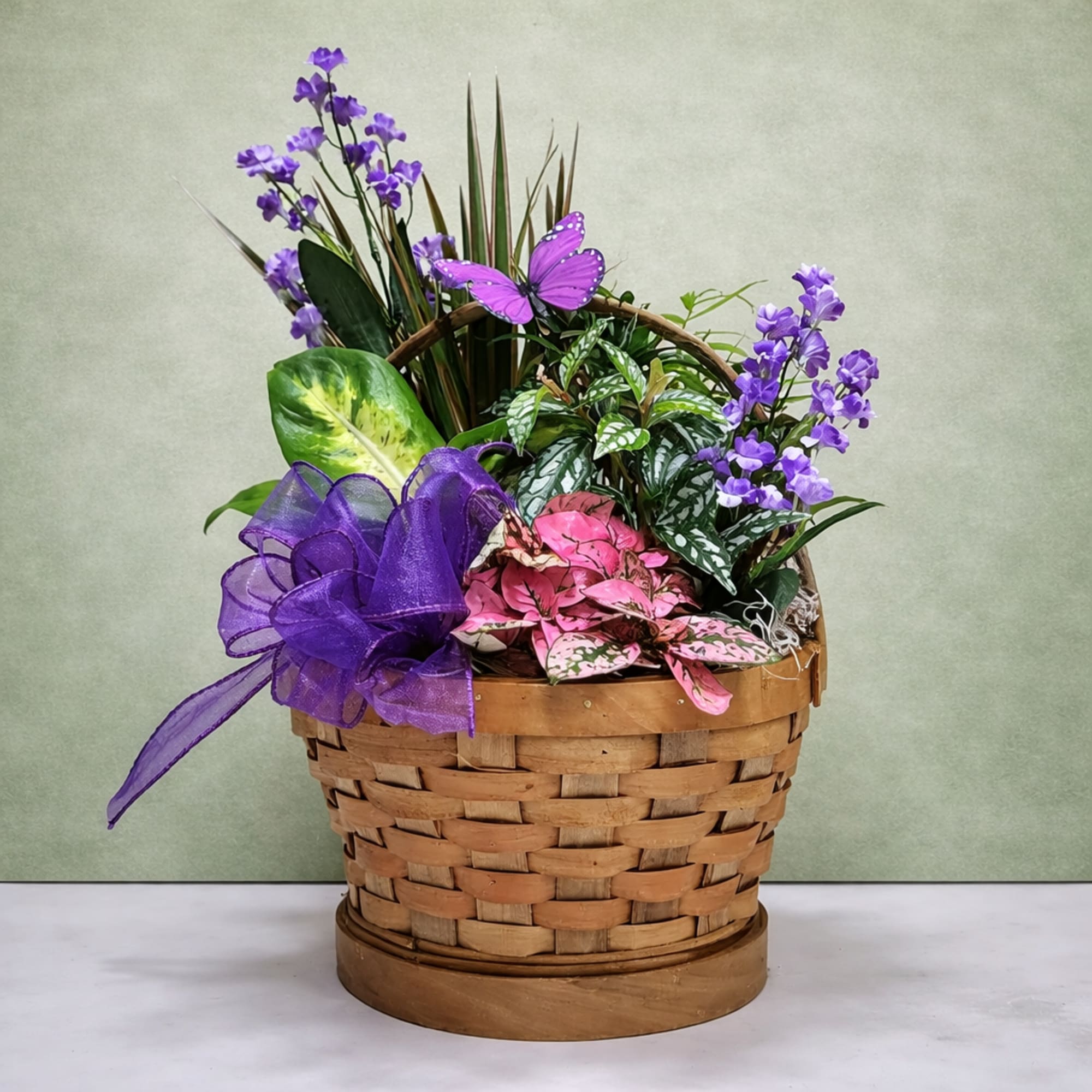 Purple flowers and mixed foliage arranged in a woven basket with a ribbon.