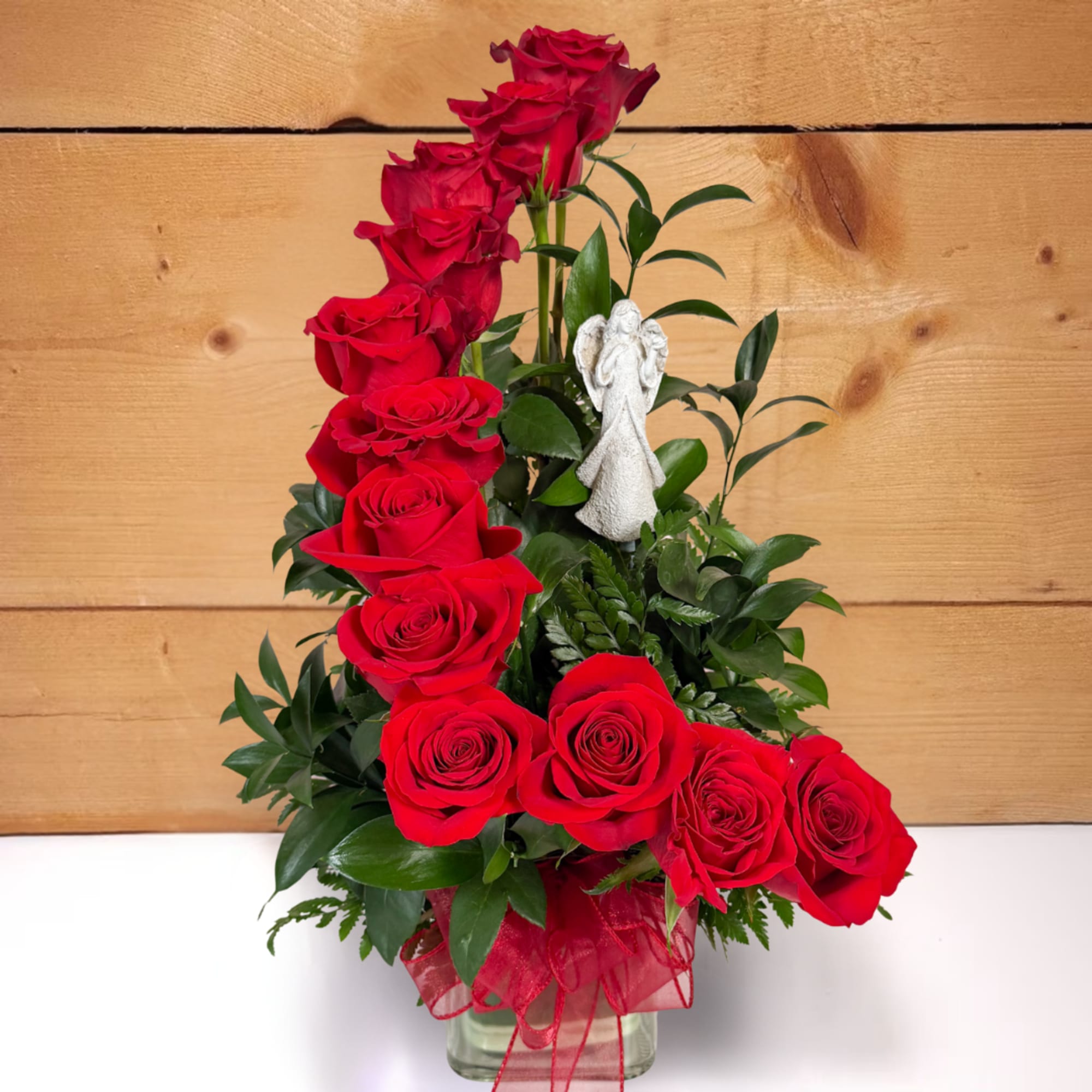 Red roses arranged in a clear vase with a small angel figurine