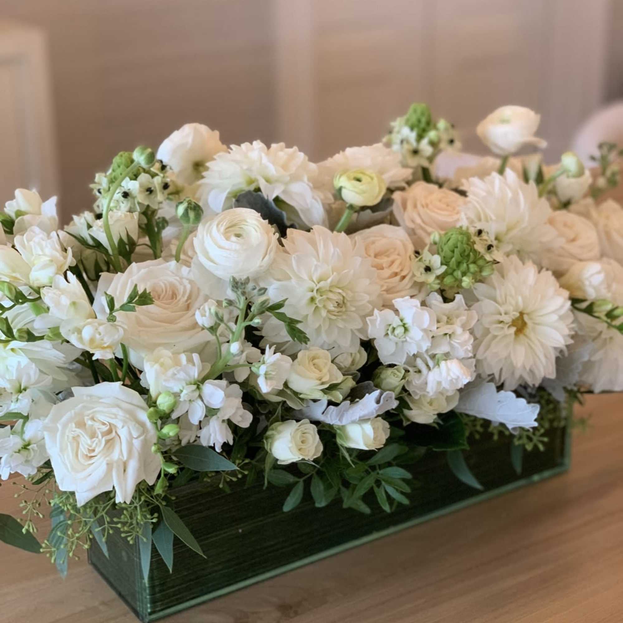 Closely packed white and cream-toned roses, dahlias and ranunculus sit amid sprays