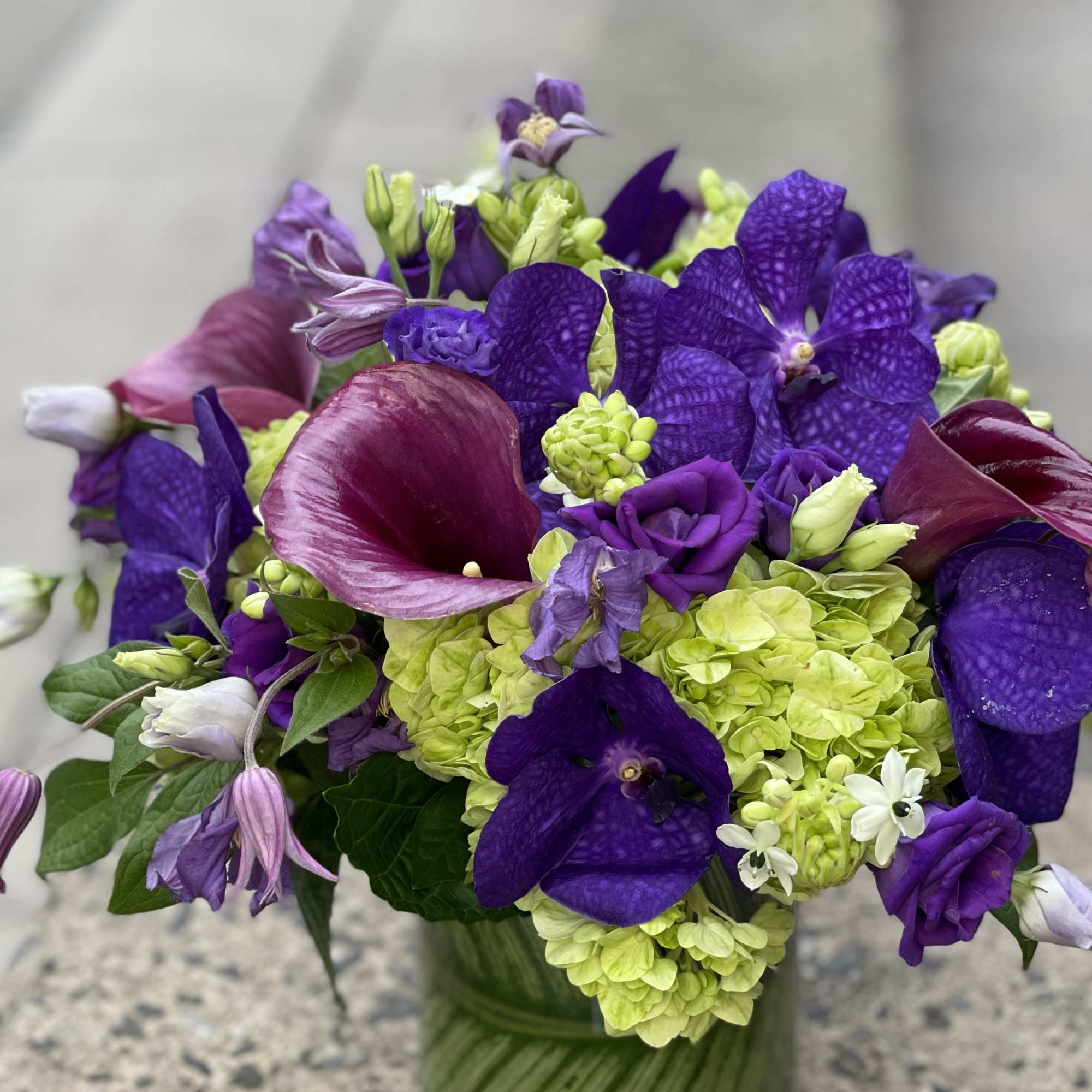 Purple and green floral arrangement in a glass vase
