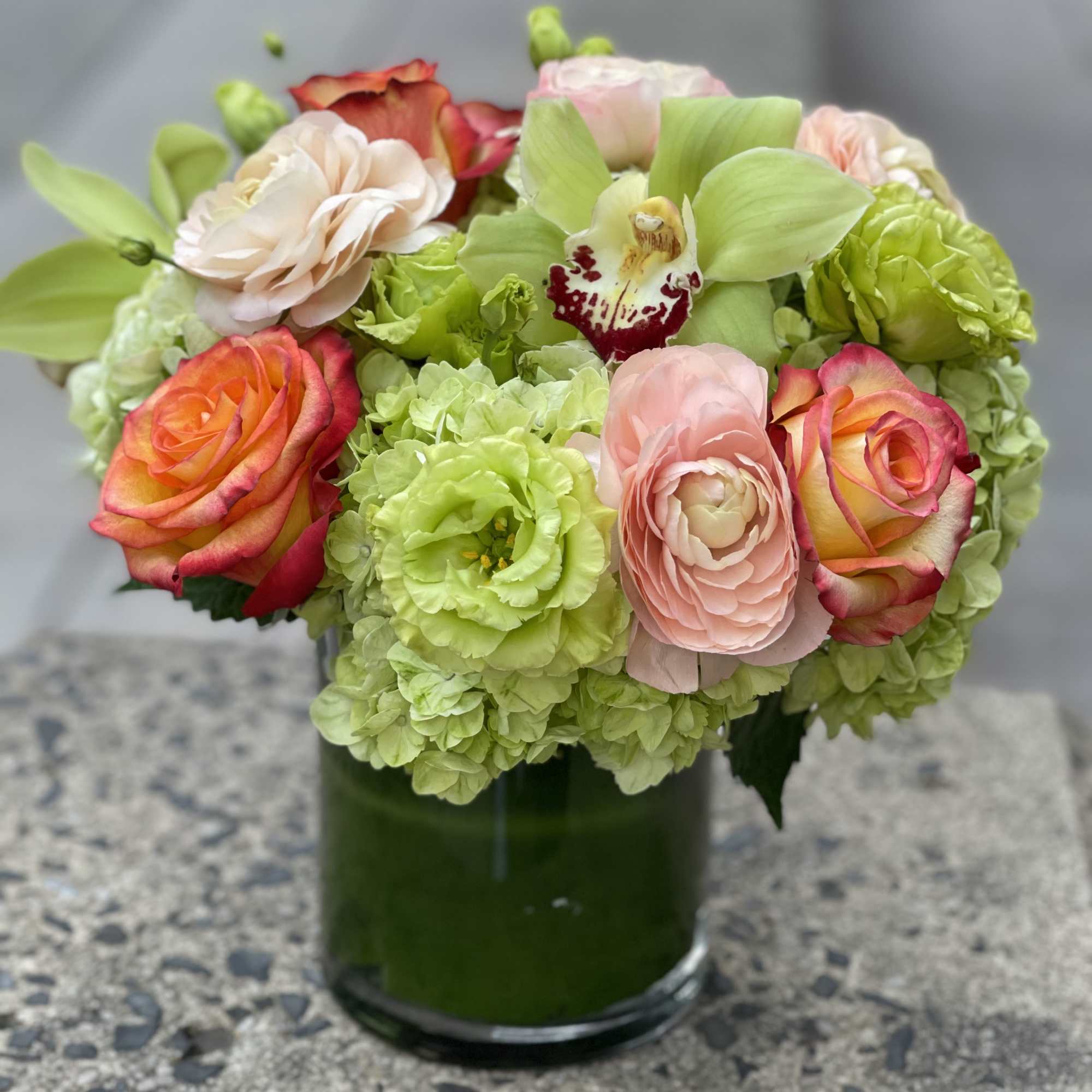 Mixed bouquet of roses, hydrangeas, and orchids in a green glass vase