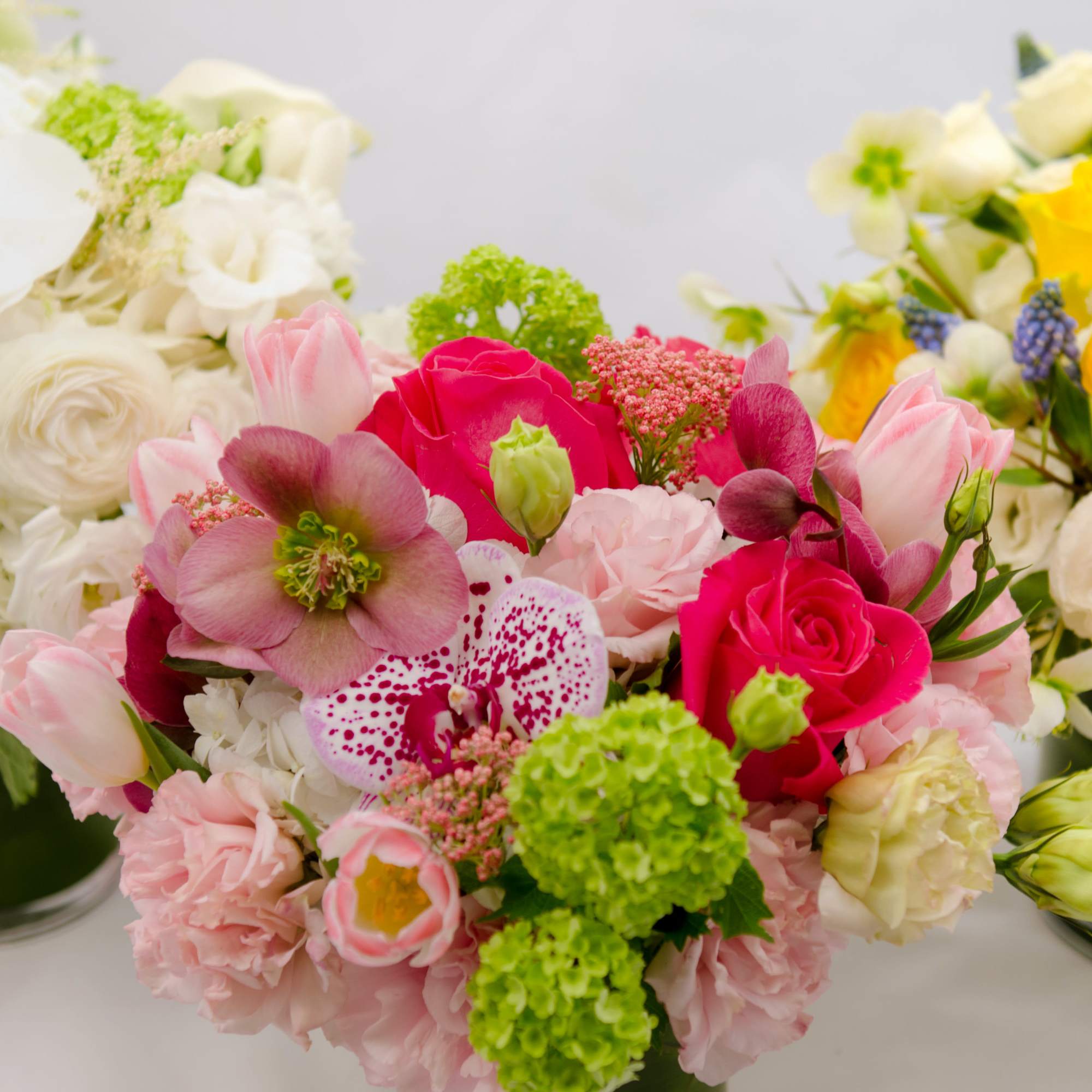 Three colorful floral arrangements in glass vases, including pink, white, and yellow blooms