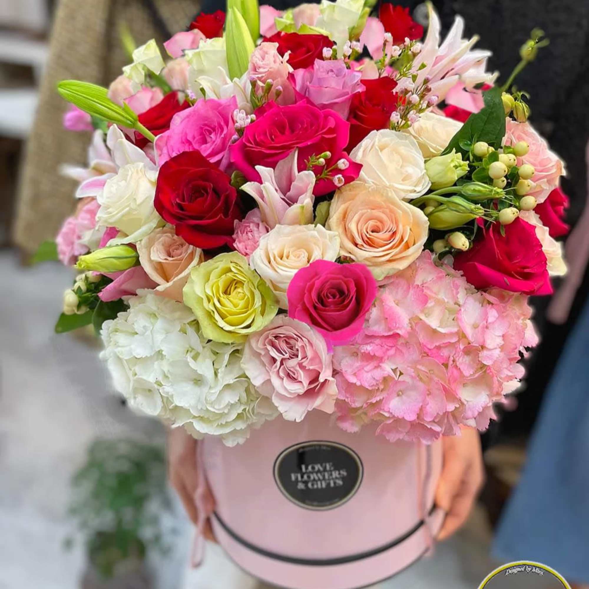 Large pink hat box arrangement of pink, red, and cream roses with lilies and hydrangeas.