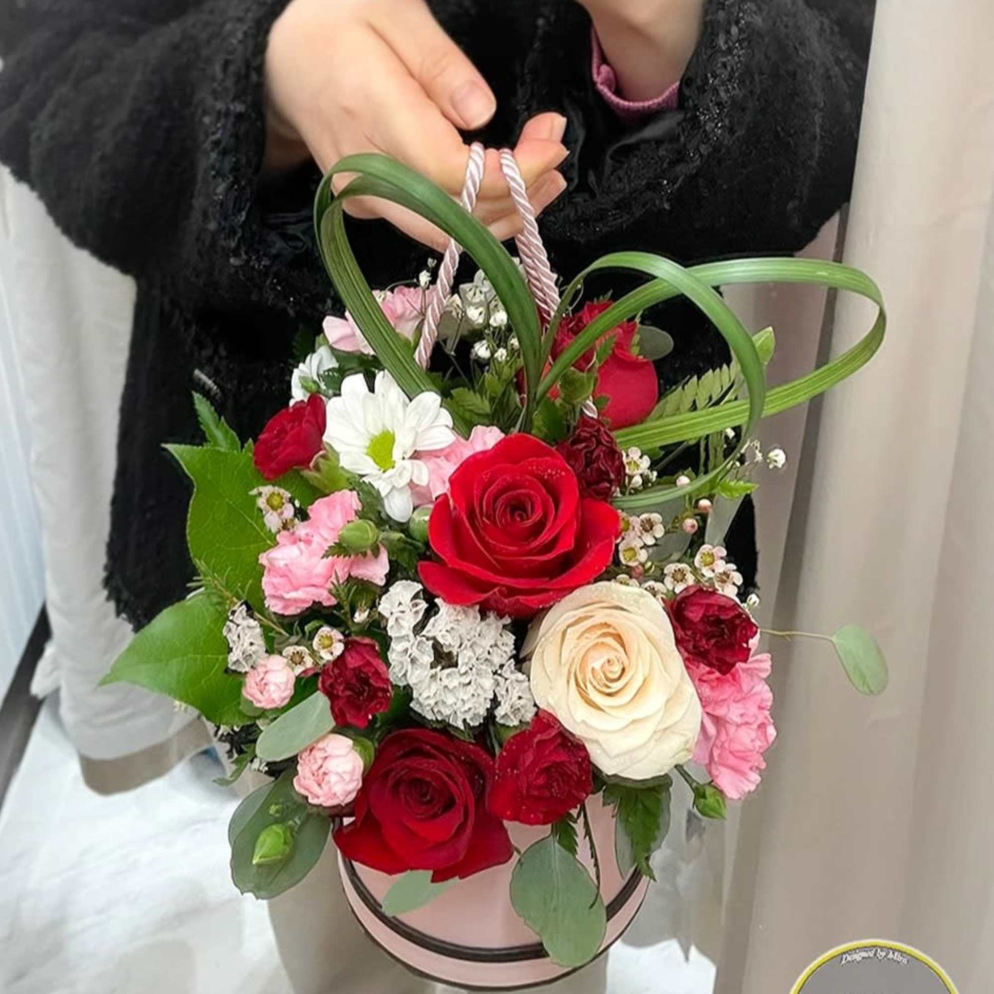 Round pink hatbox arrangement of red and cream roses with pink and white accent flowers