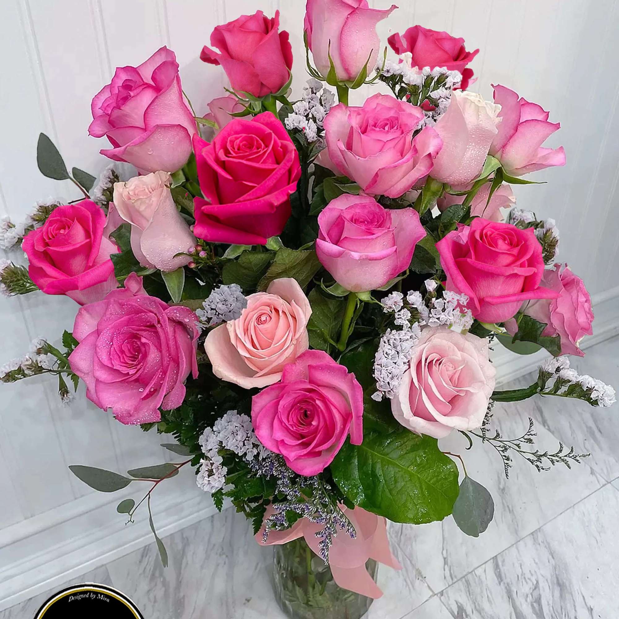 Tall glass vase of hot pink and light pink roses with white filler flowers and a pink ribbon