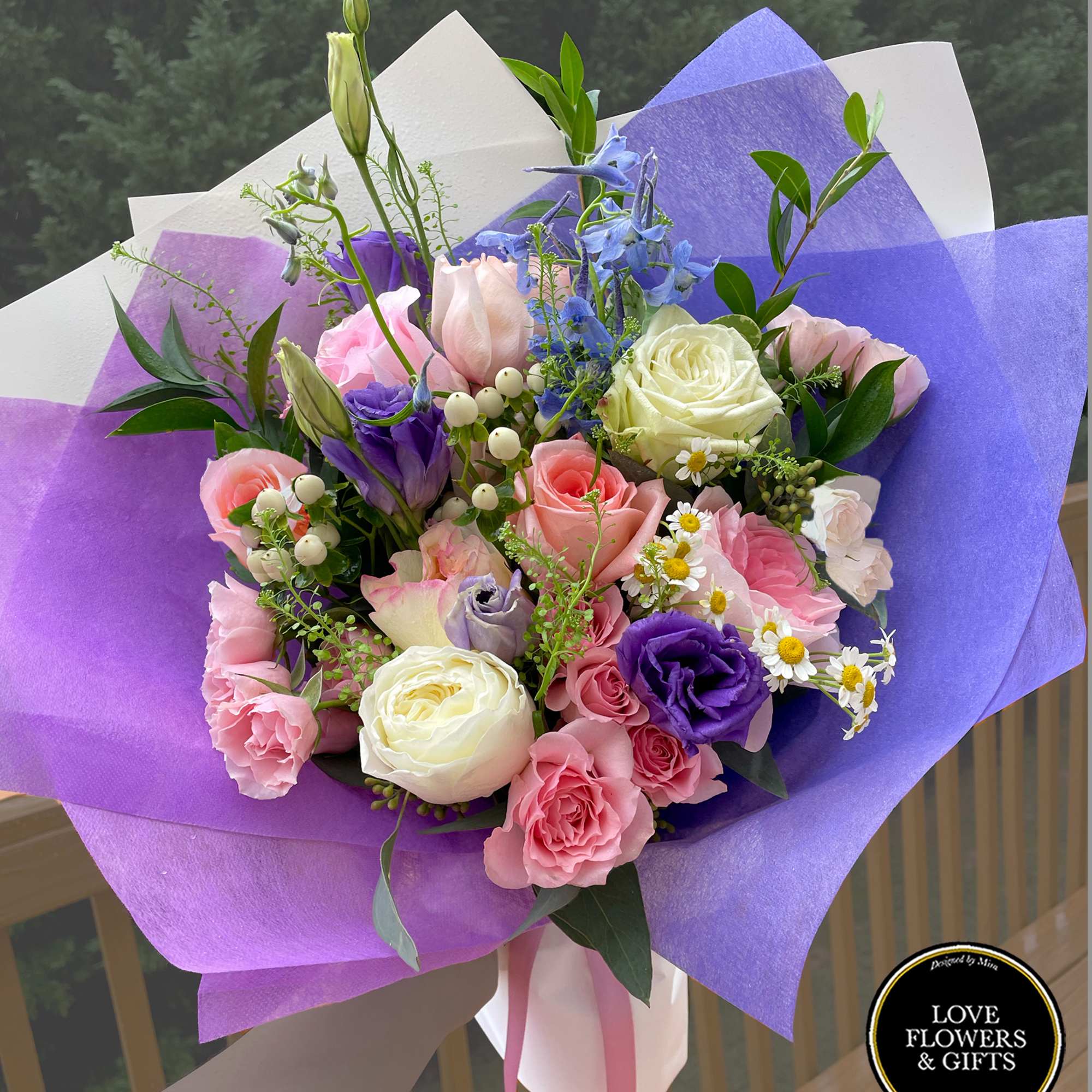 Hand-tied bouquet of pink roses, purple lisianthus, and white blooms wrapped in purple and white paper