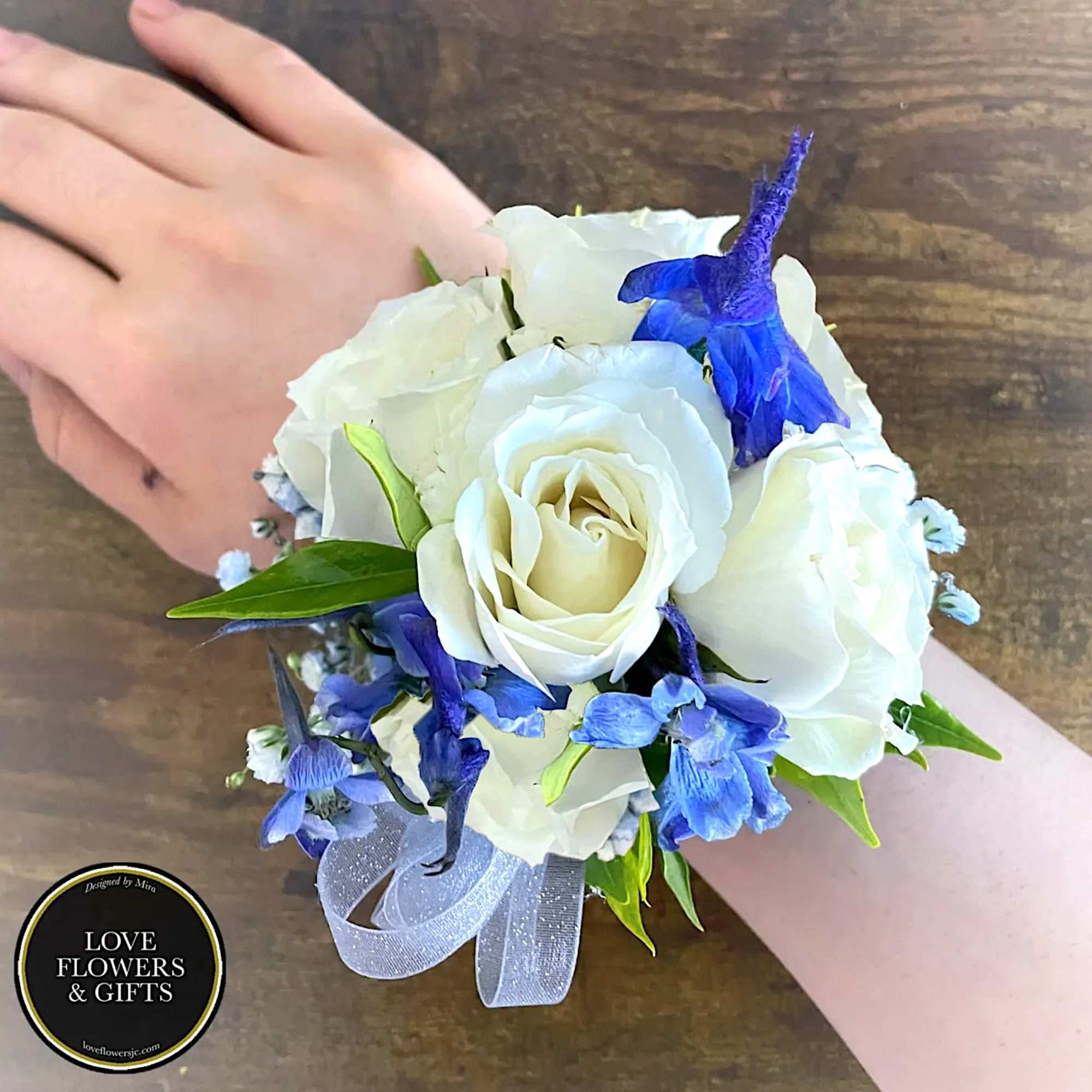 White rose and blue flower wrist corsage with ribbon on a person’s wrist