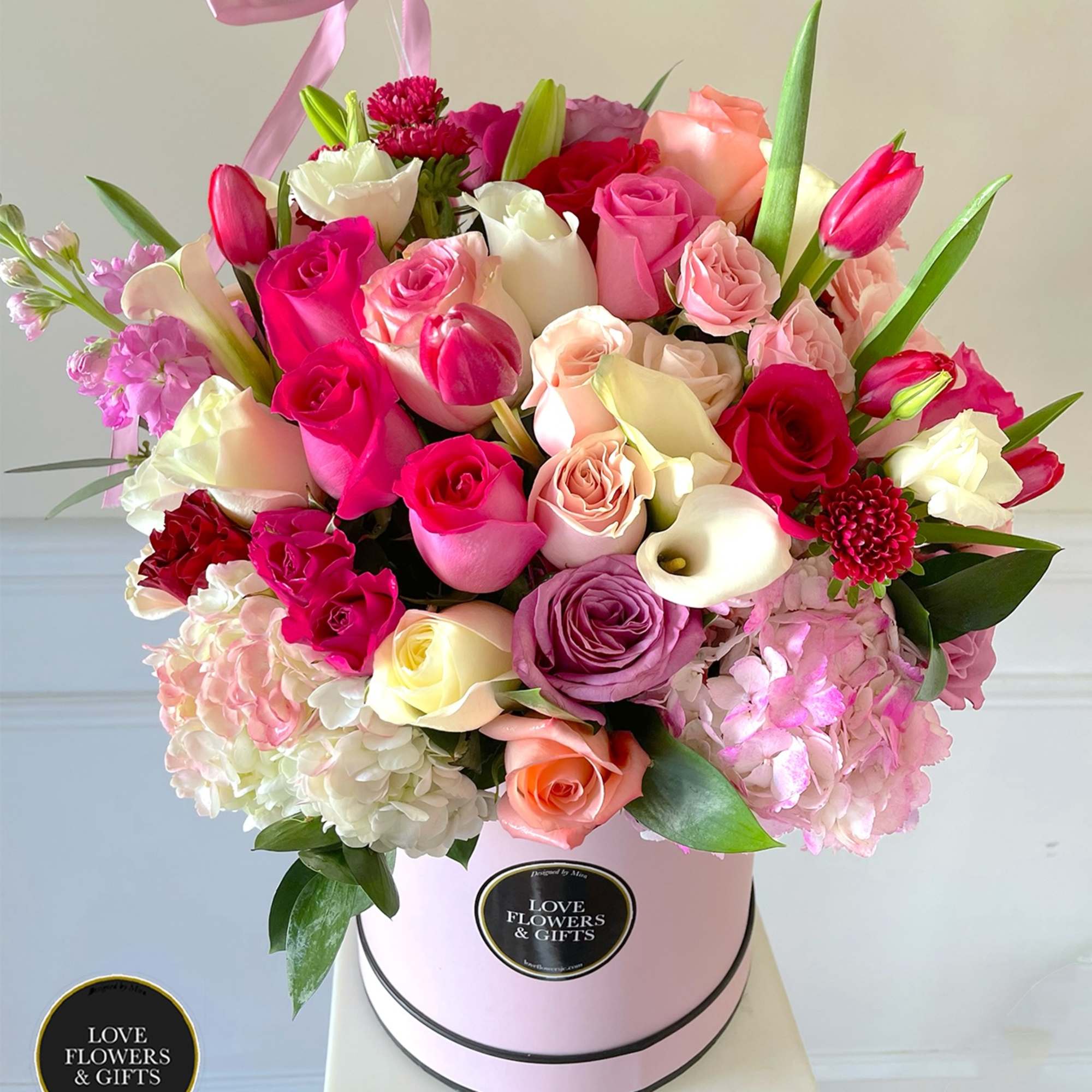 Round hatbox arrangement of mixed pink, white, and peach roses with tulips and calla lilies.