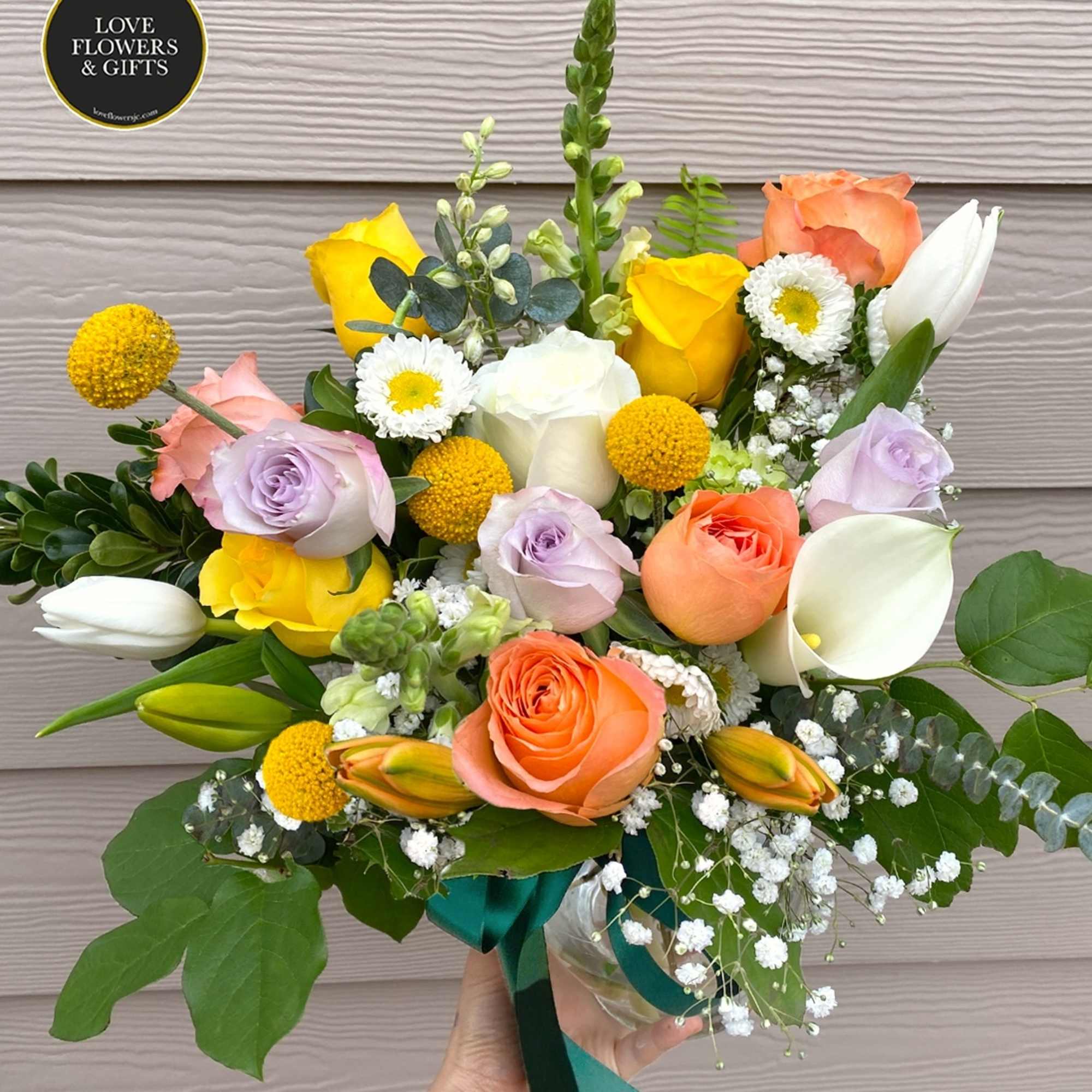 Hand-tied bouquet of yellow, white, orange and lavender flowers arranged in a small glass vase.