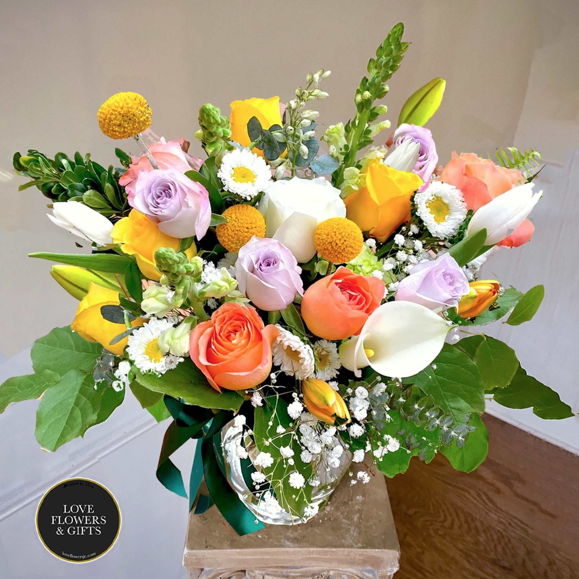 Mixed bouquet of yellow, peach, and lavender flowers with white calla lilies in a clear glass vase