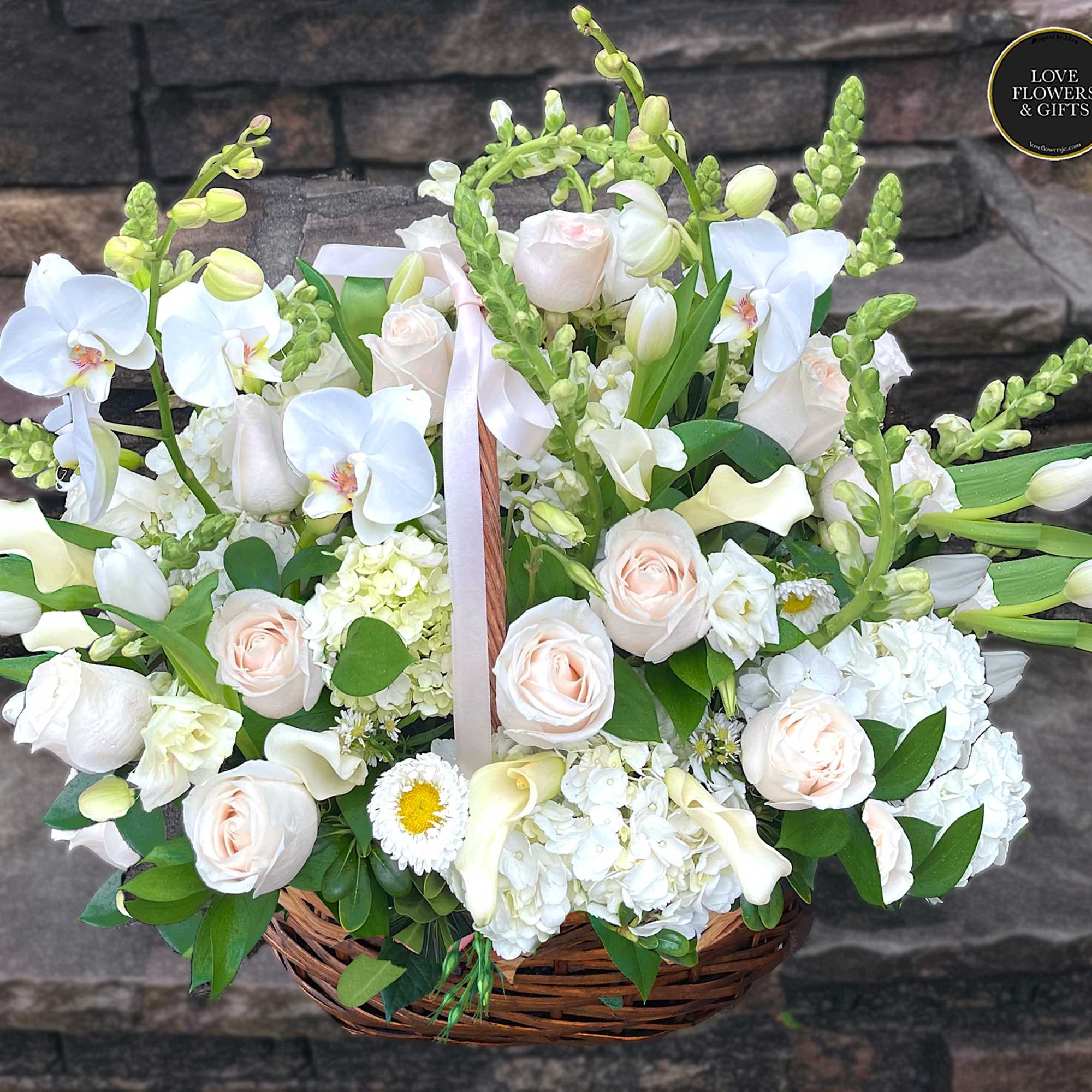 Large basket of white orchids, roses, hydrangeas and calla lilies with soft peach accents.