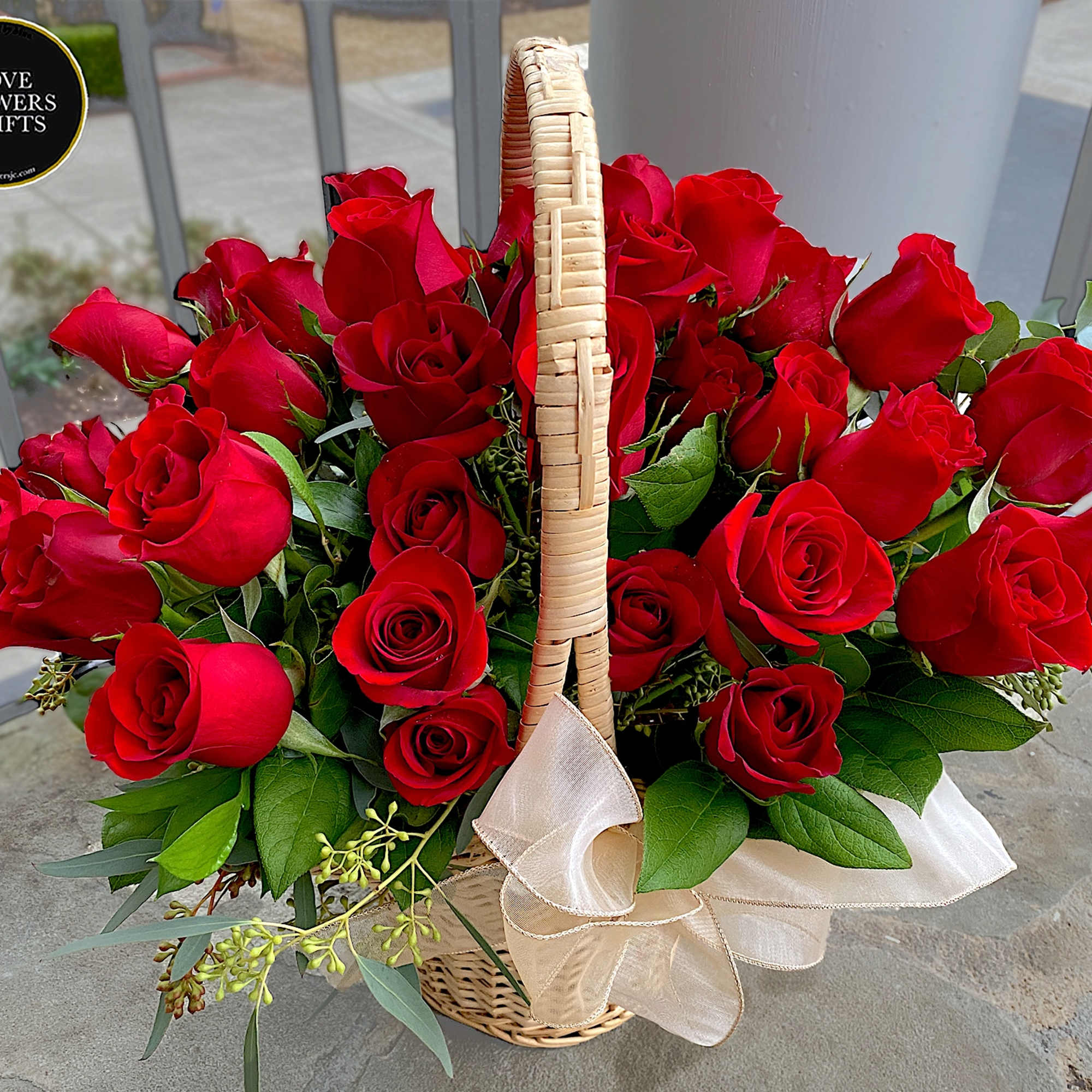 Wicker basket overflowing with red roses and a cream ribbon bow.