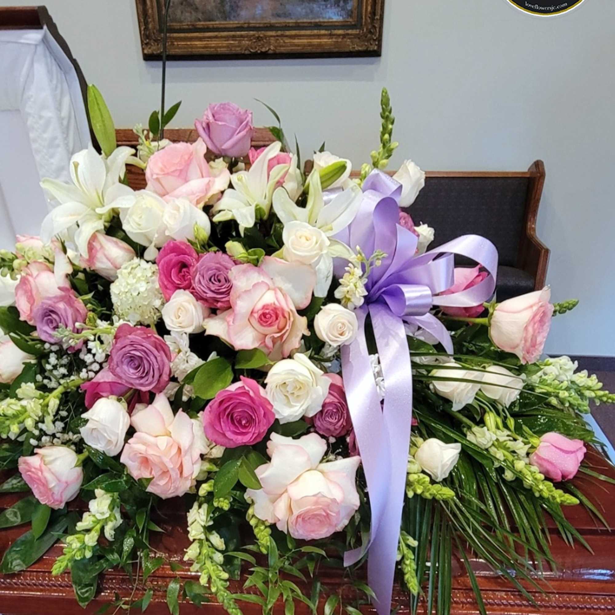 Pink, lavender, and white rose and lily casket spray with a lavender ribbon.