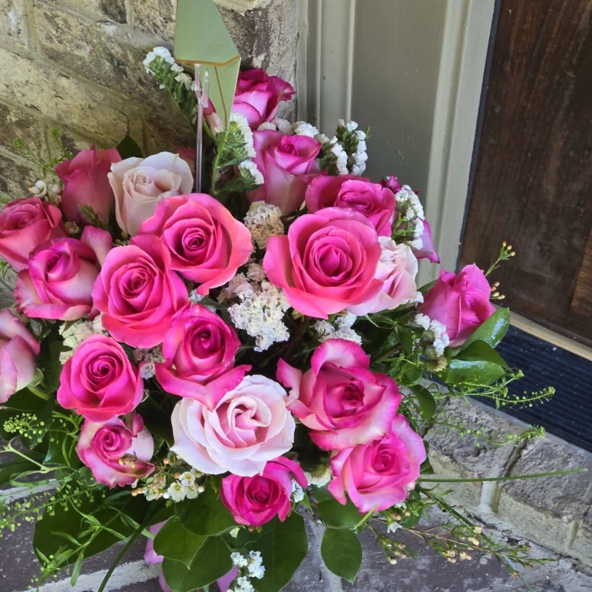 Arrangement of bright and pale pink roses with white filler flowers in a glass vase