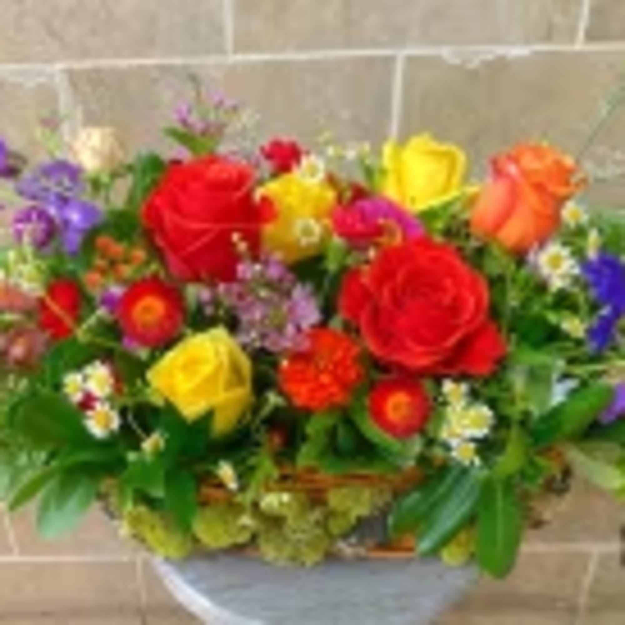 Low rectangular arrangement of red, yellow, and orange roses with mixed bright flowers in a basket