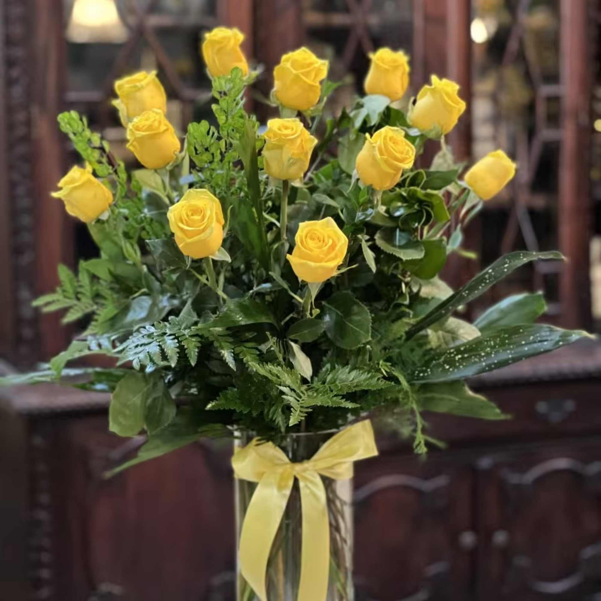 Yellow roses arranged in a clear glass vase with a yellow ribbon
