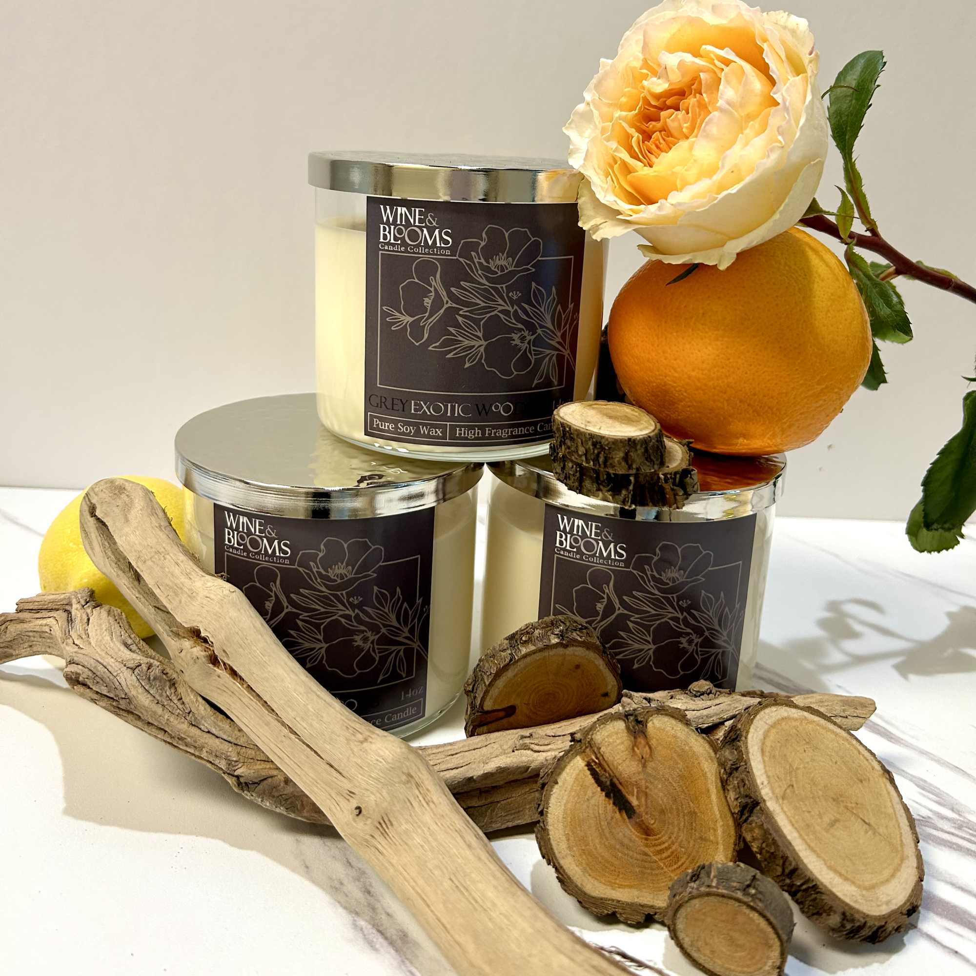 Three candles with an orange rose and citrus fruit accents