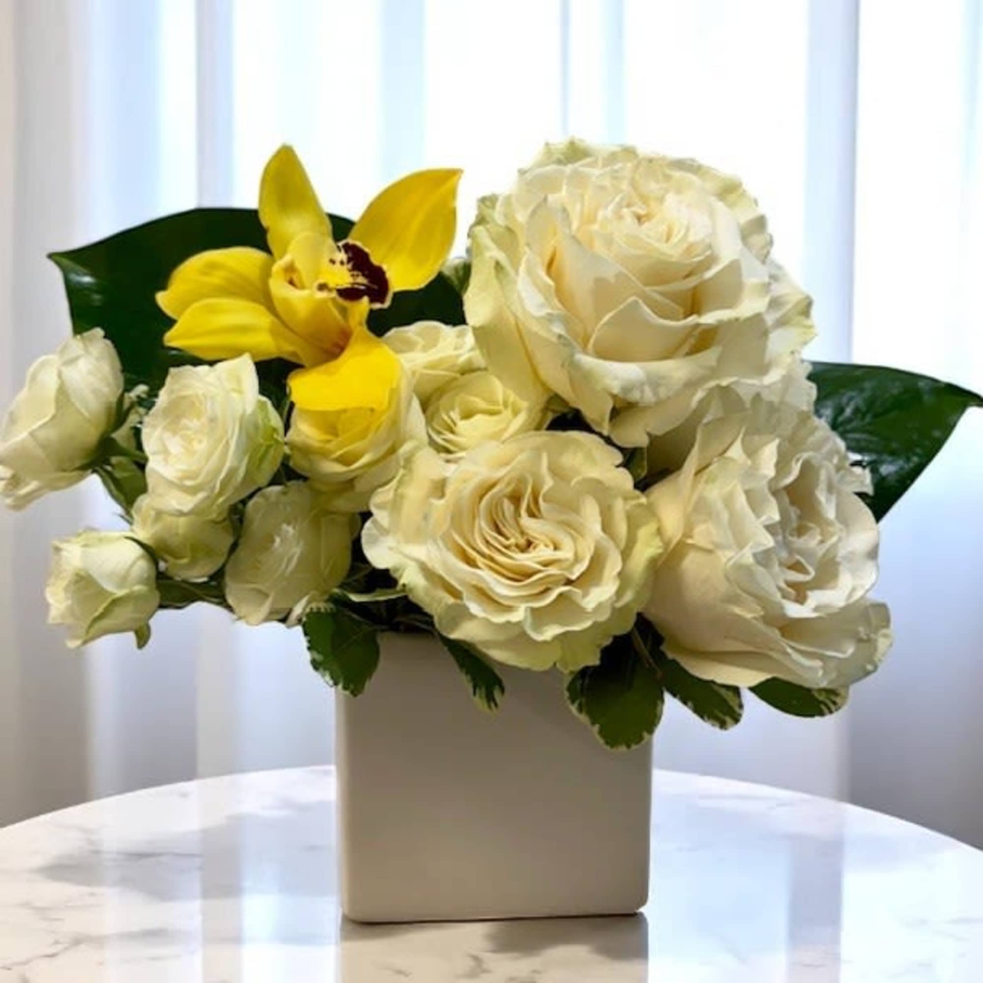 Cream roses and a yellow orchid in a white vase