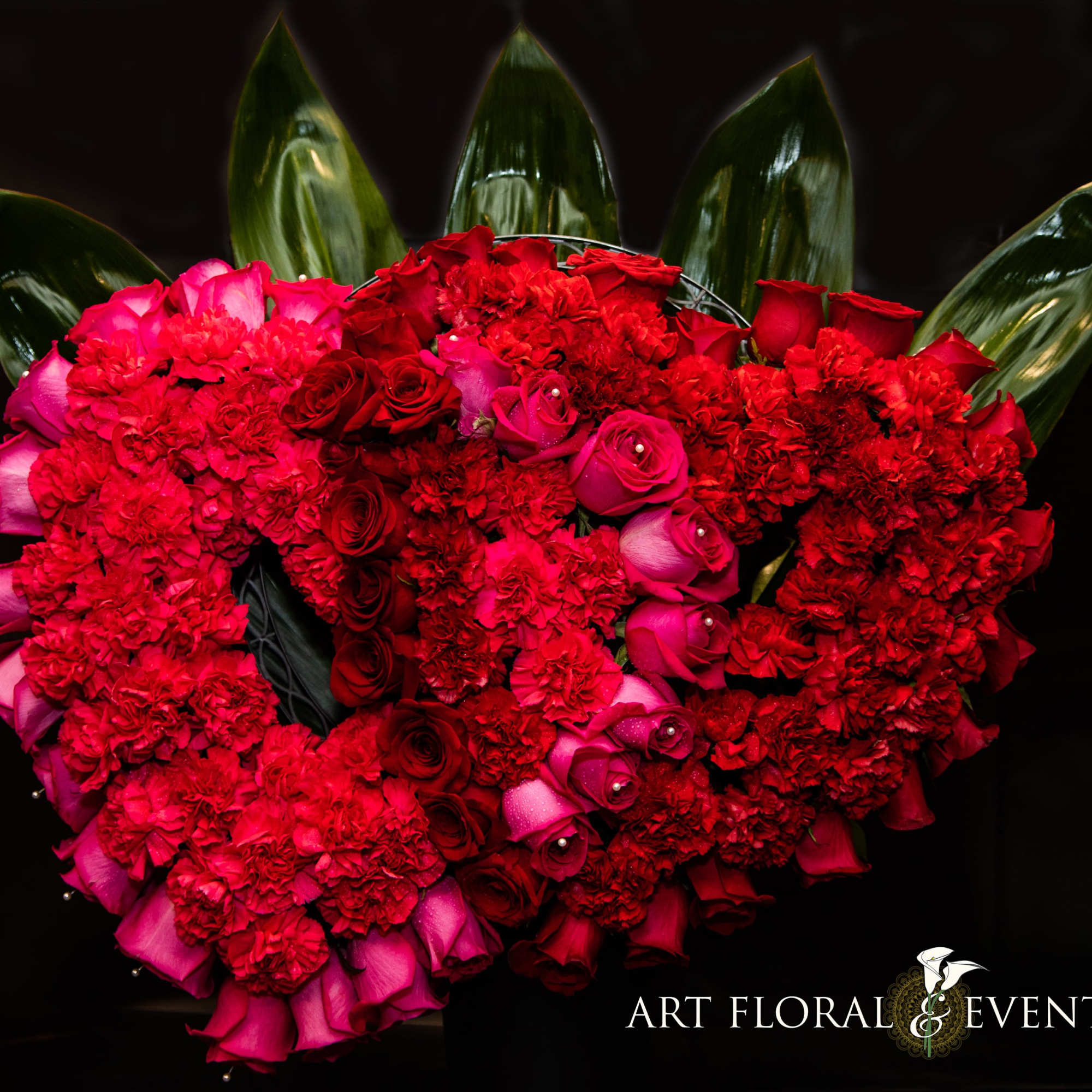 Heart-shaped bouquet of red and pink roses with dark green leaves