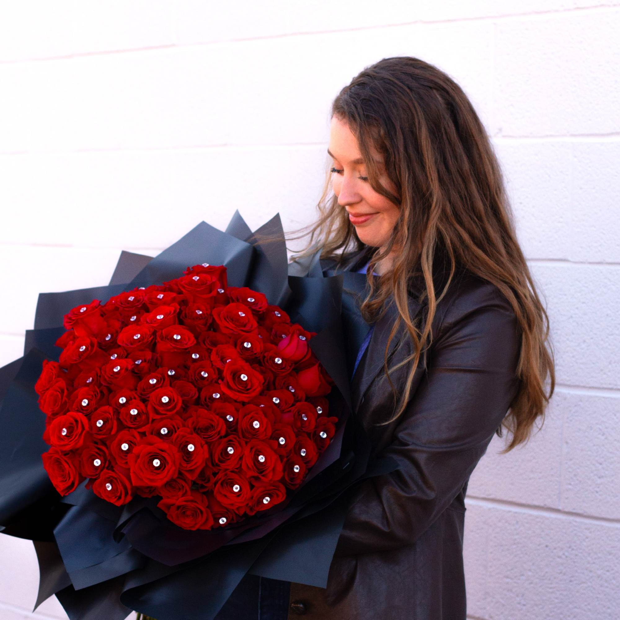 Woman holding a large bouquet of red roses wrapped in black paper