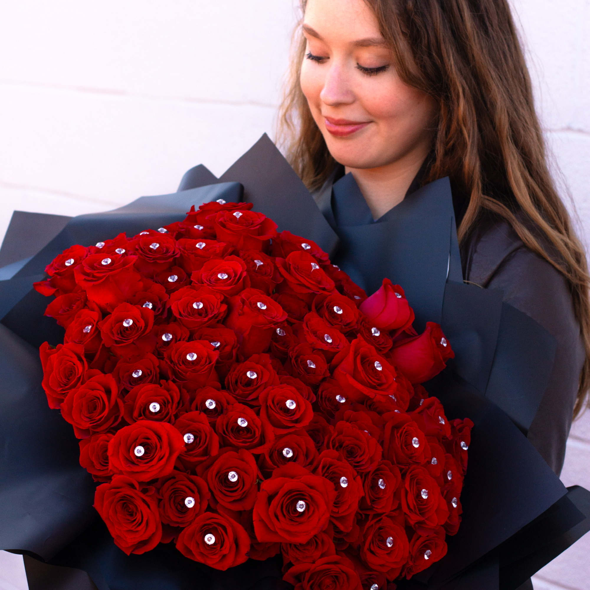 Woman holding a large bouquet of red roses wrapped in dark paper