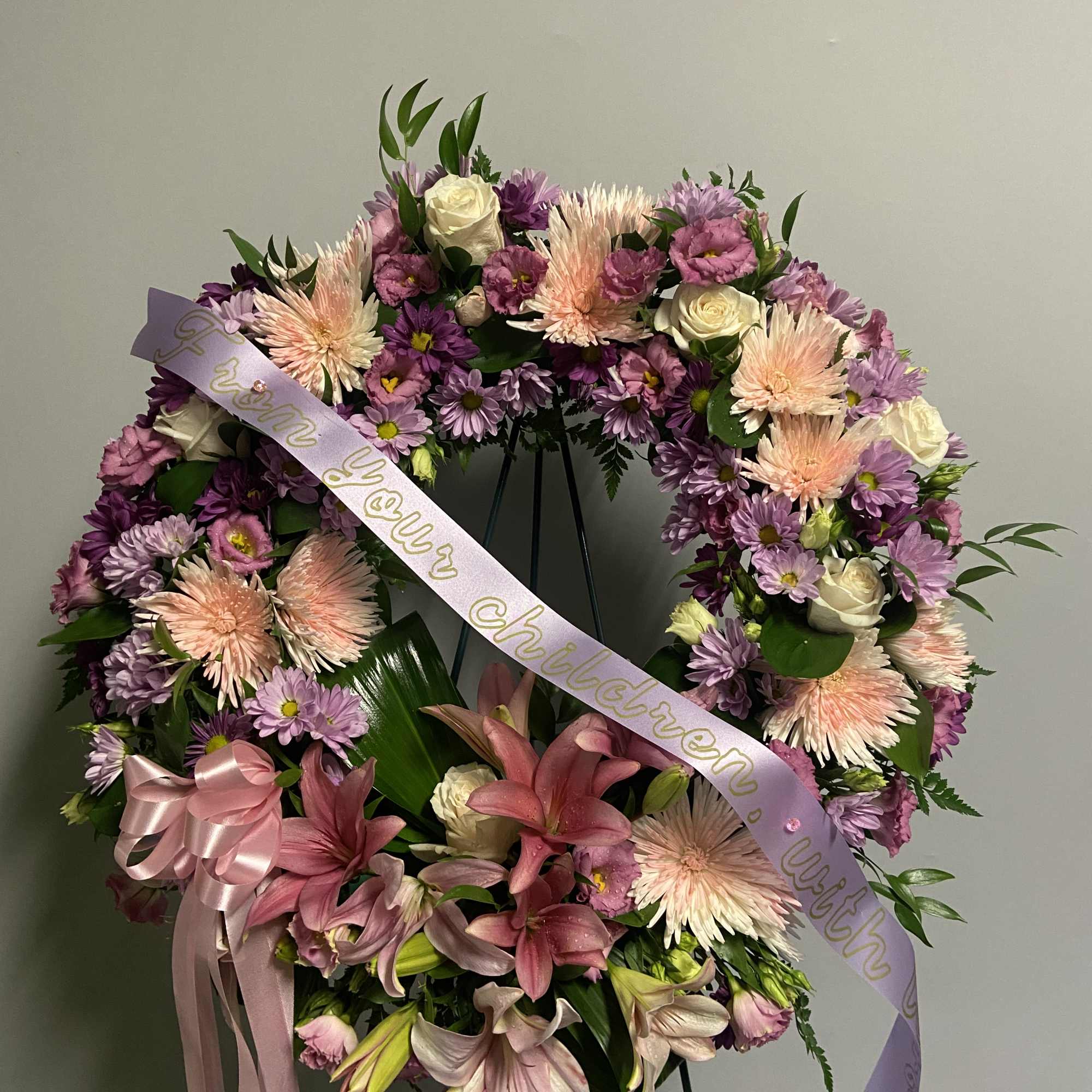 Large purple and pink funeral wreath with lilies and roses on a stand