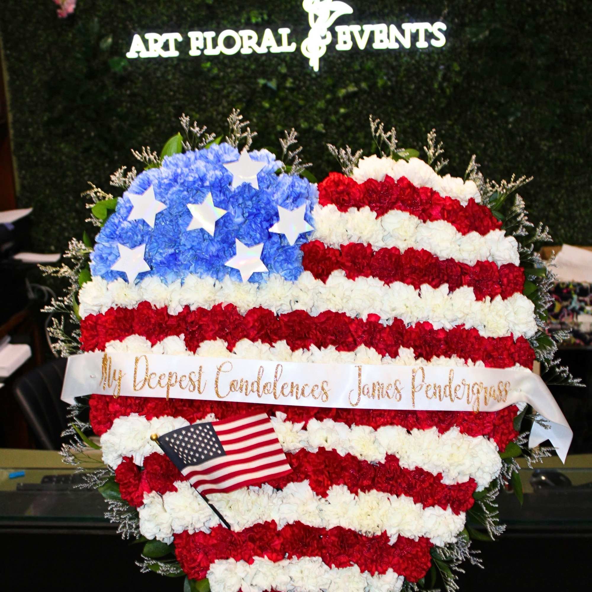 Heart-shaped red, white, and blue floral tribute with a small American flag