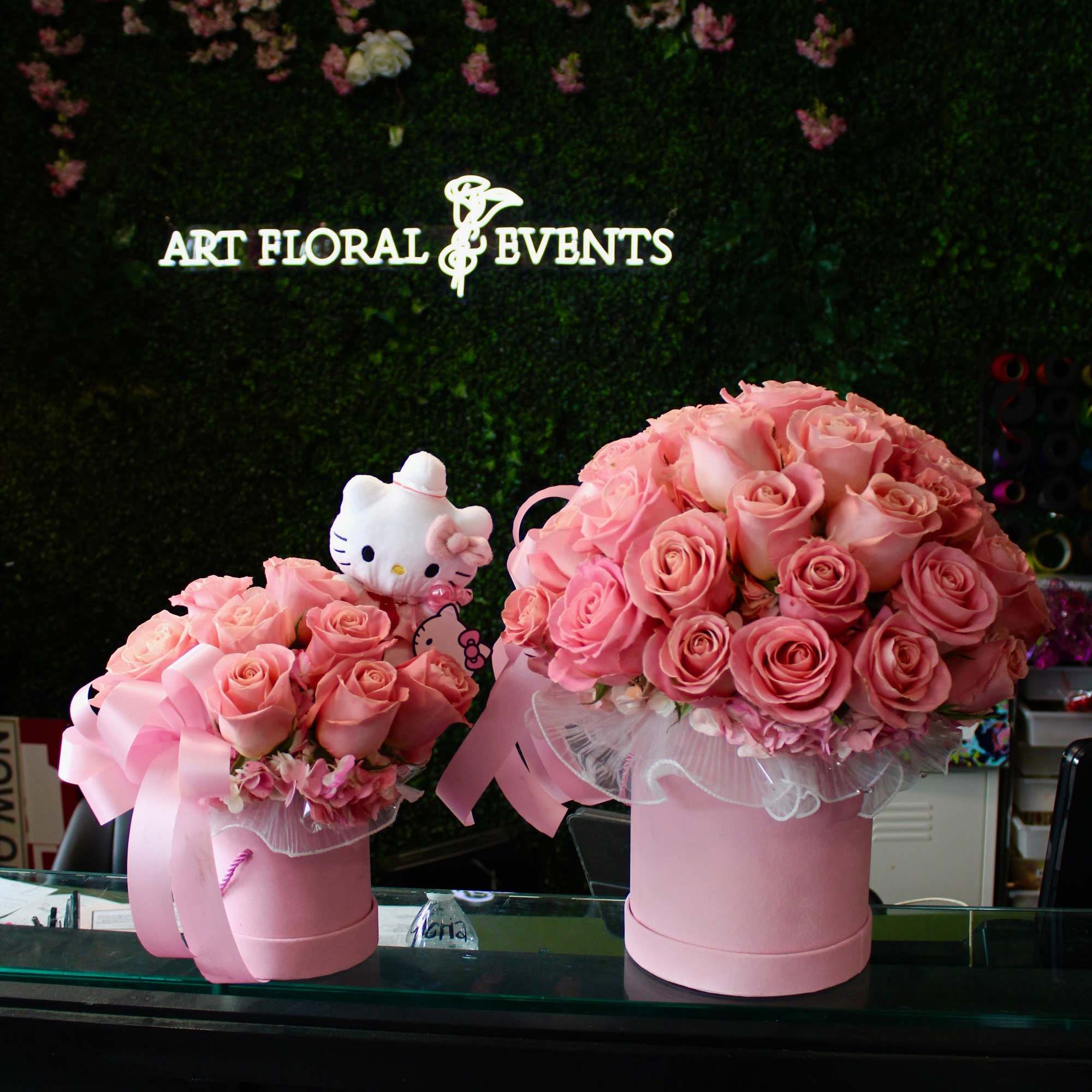 Two pink rose arrangements in round boxes, one with a Hello Kitty plush