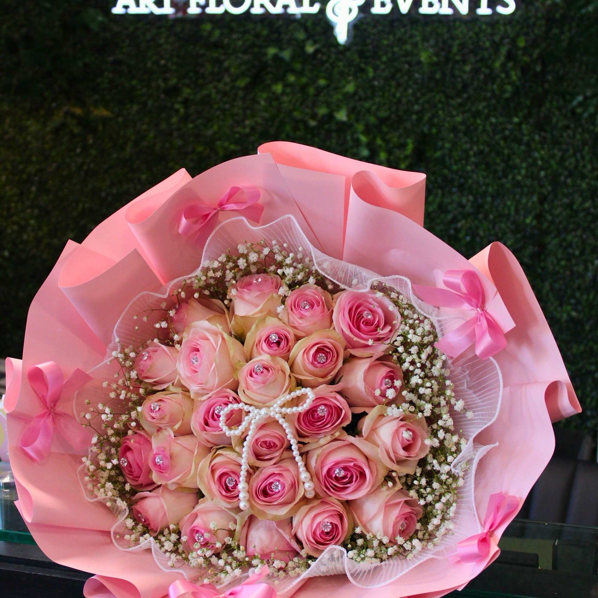 Pink rose bouquet wrapped in pink paper with ribbon and pearl accents