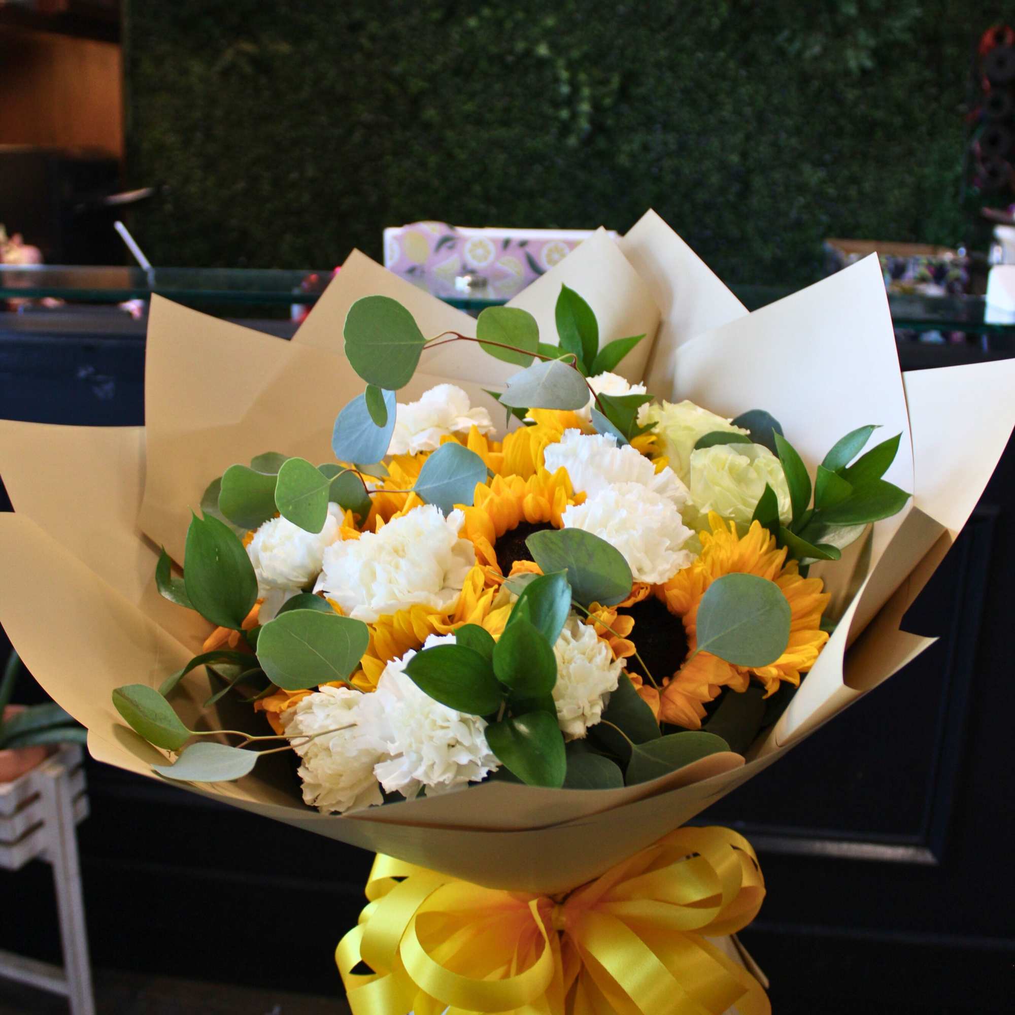 Bouquet of yellow sunflowers and white carnations wrapped in tan paper
