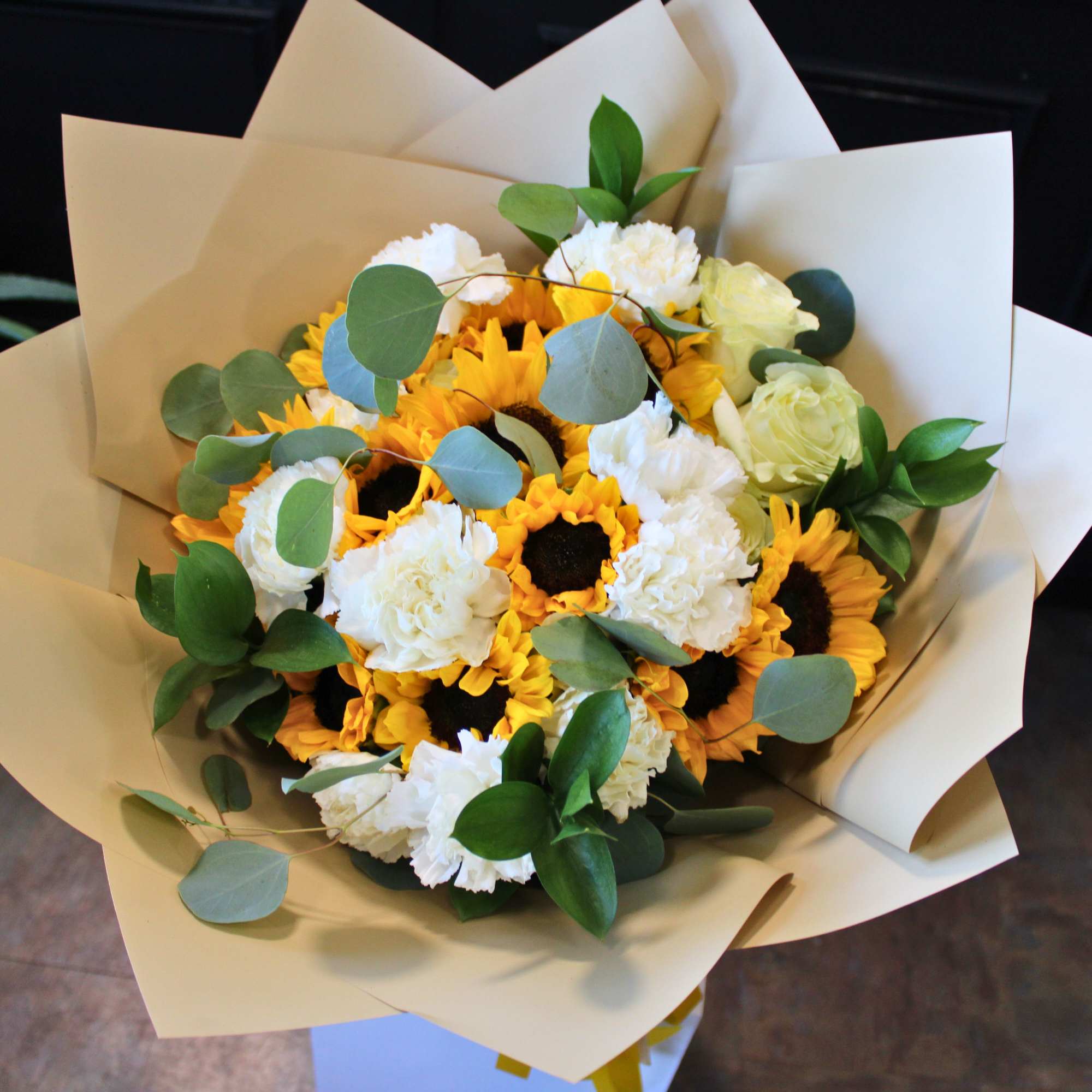 Bouquet of sunflowers and white carnations wrapped in beige paper