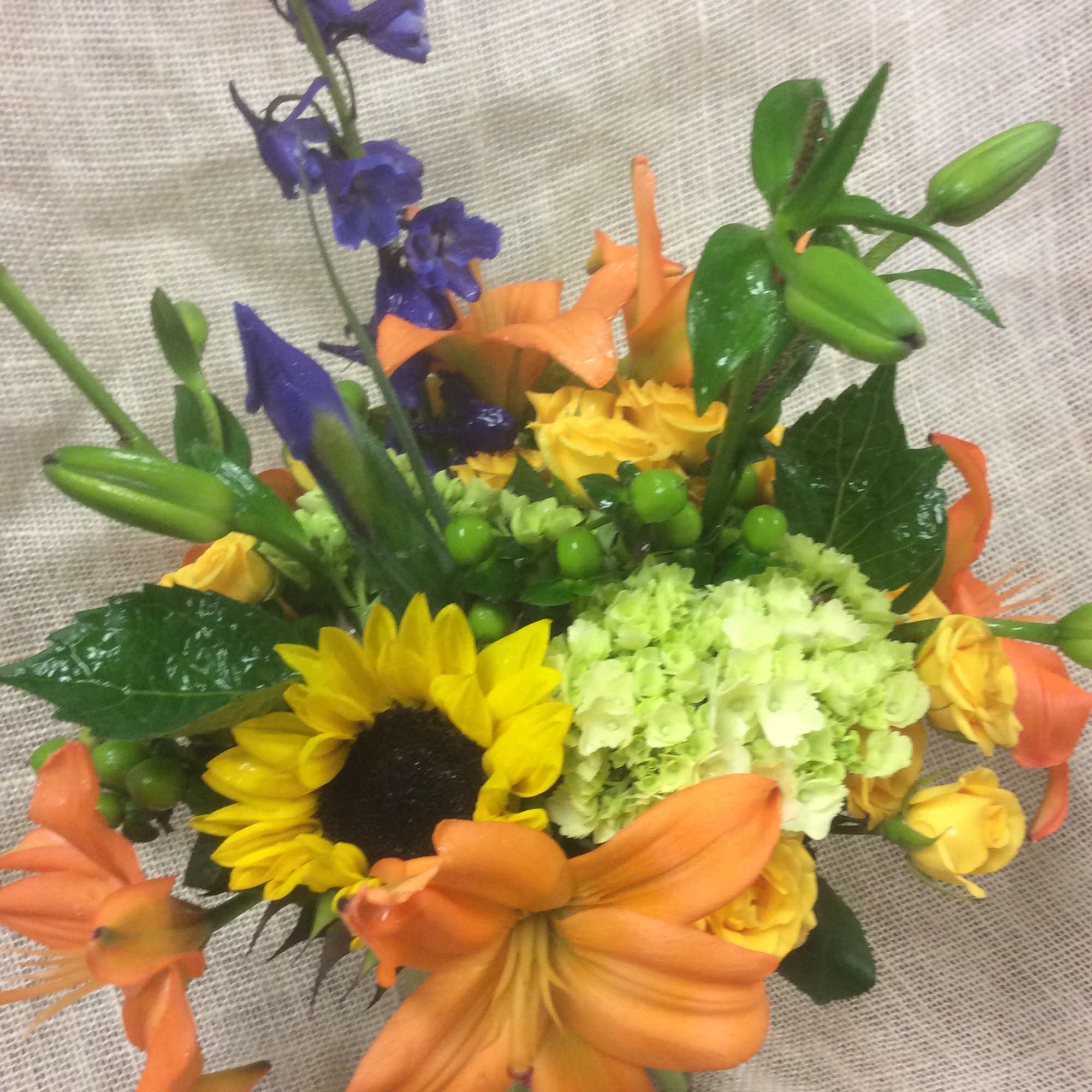 Colorful bouquet with sunflowers, lilies, roses, and blue flowers in a glass vase