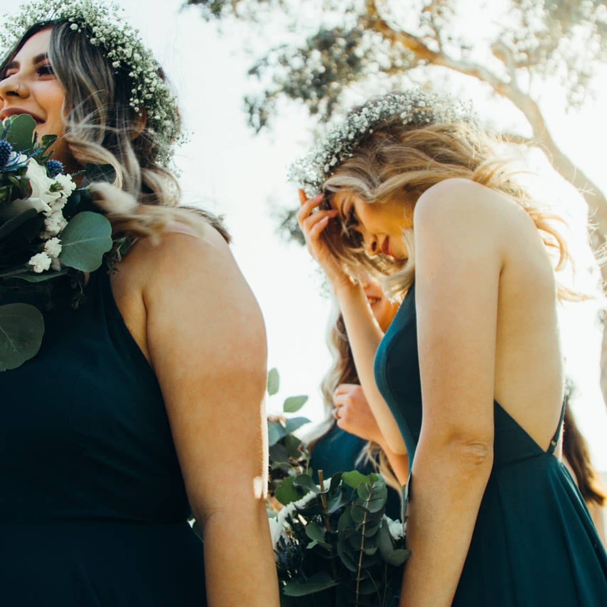 Bridesmaids in dark dresses holding bouquets and floral crowns outdoors