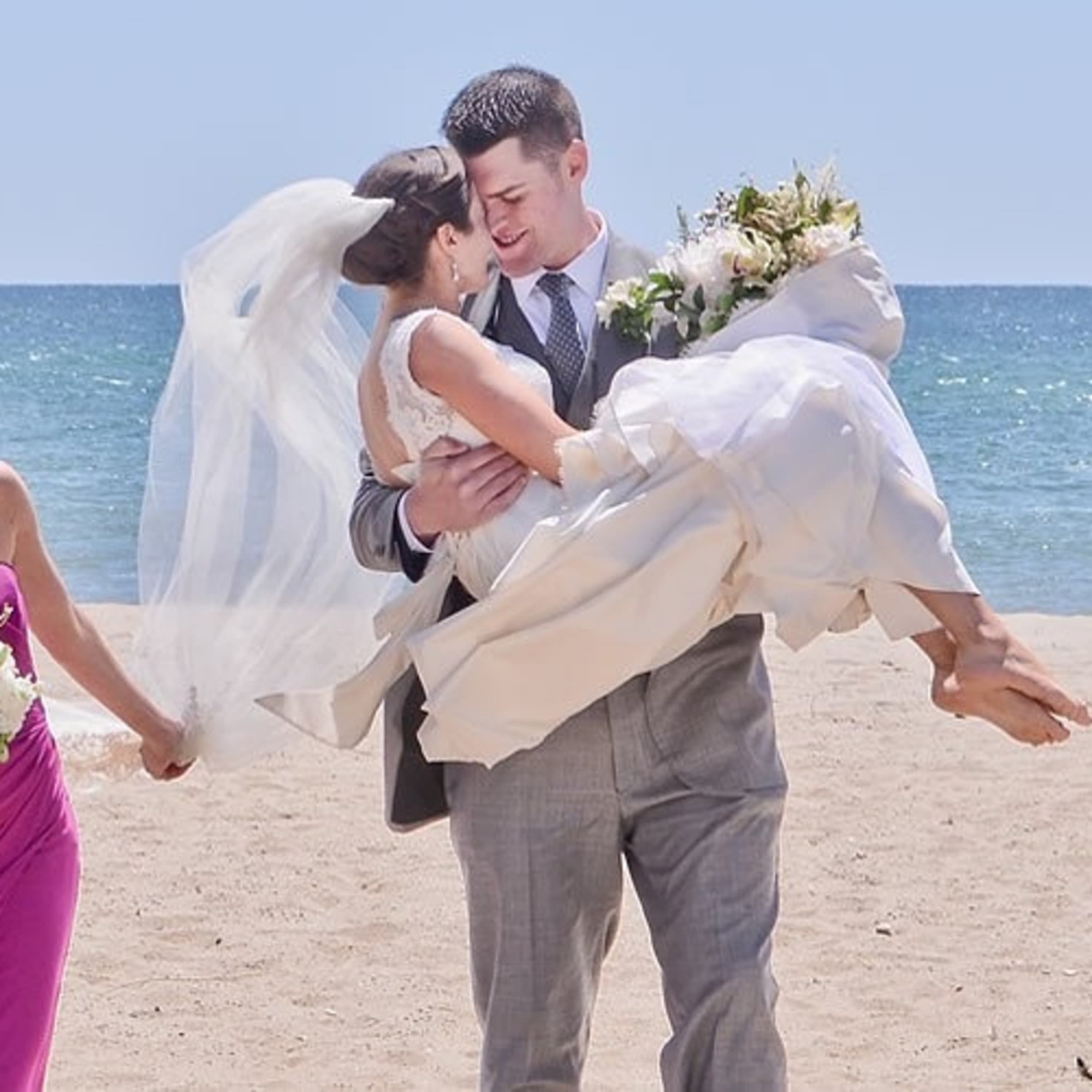 Wedding party on a beach with bridesmaids holding bouquets and the bride being carried