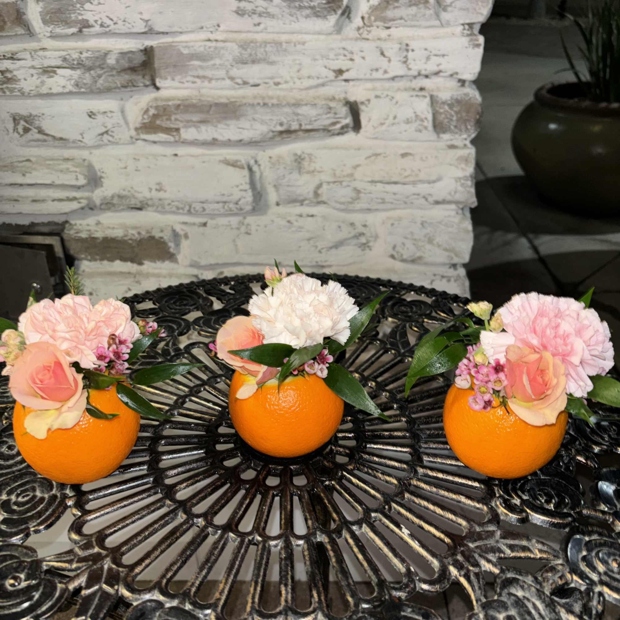 Three small floral arrangements in oranges on a black metal table