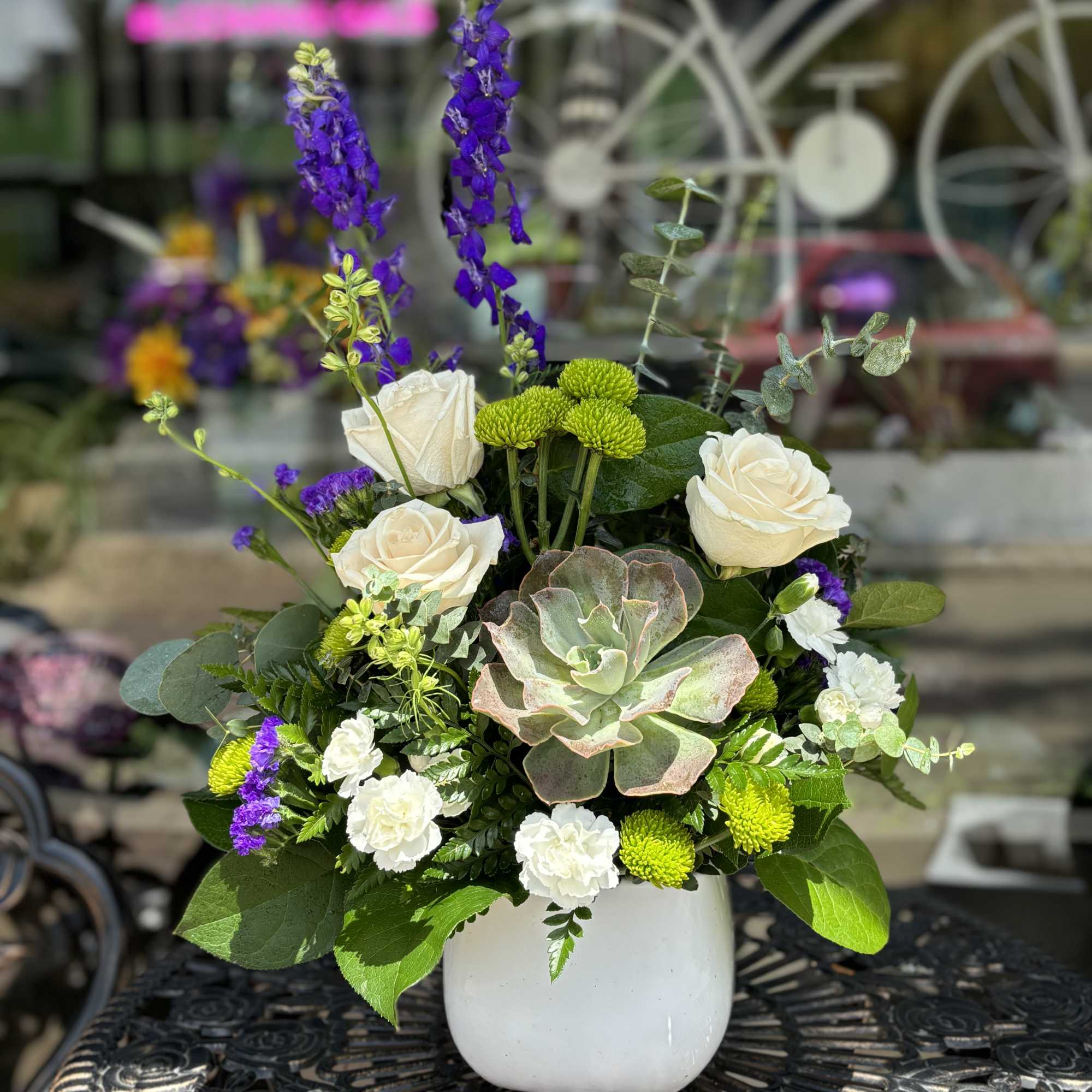 White roses and purple spikes in a white vase with a succulent centerpiece