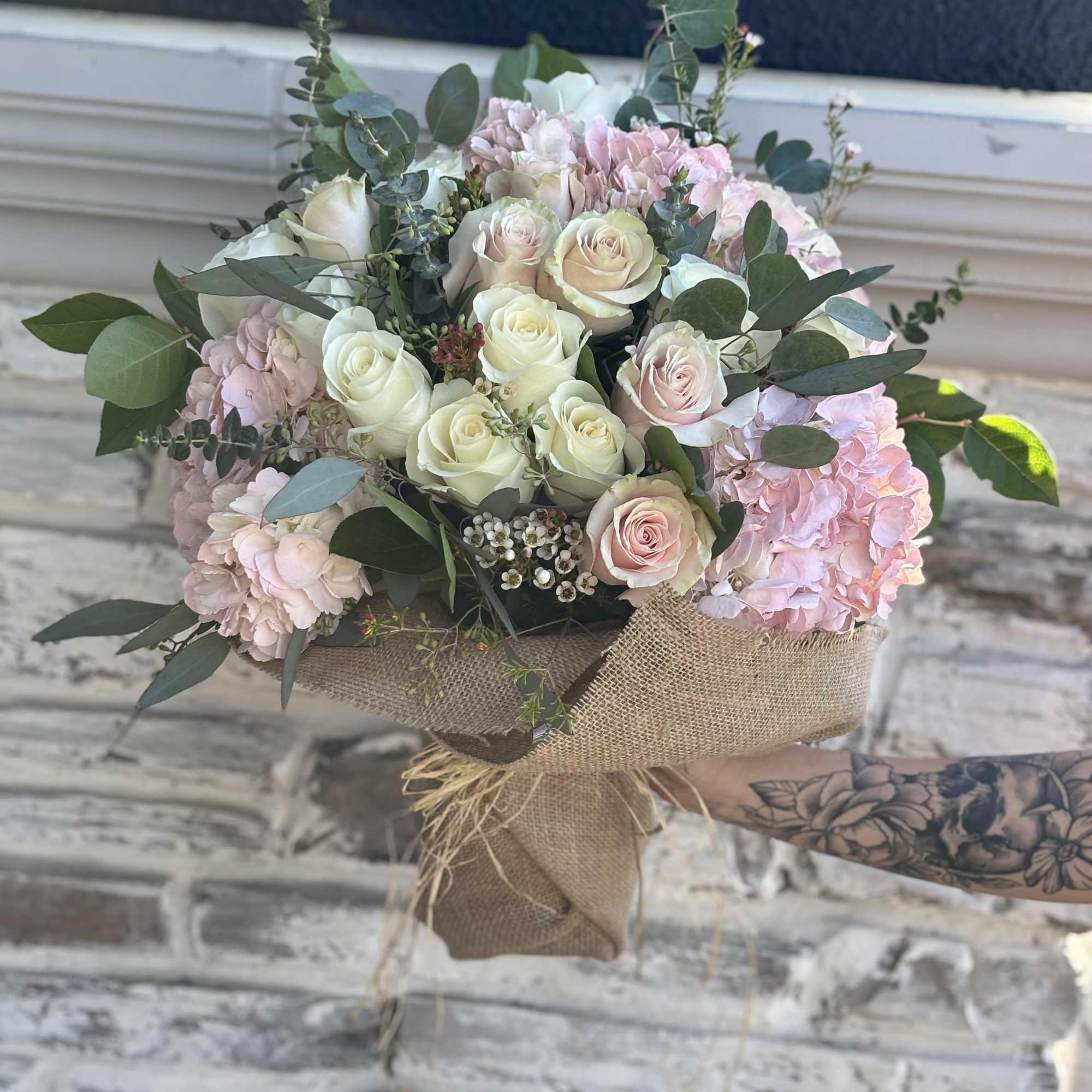 Bouquet of pale pink and white roses with hydrangeas wrapped in burlap