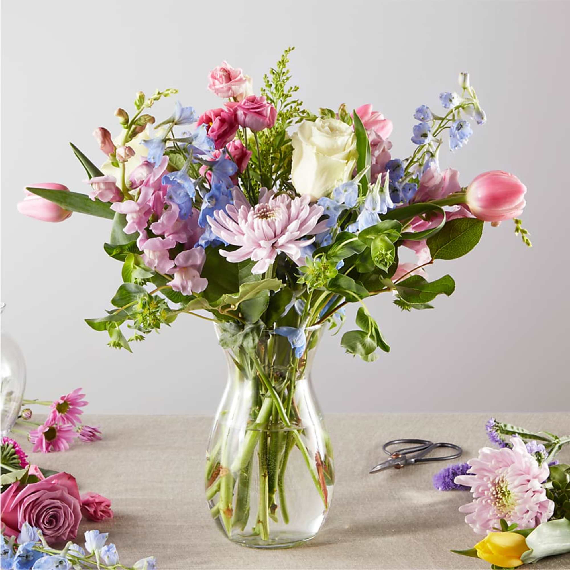 Mixed bouquet of pink, blue, and white flowers in a clear glass vase