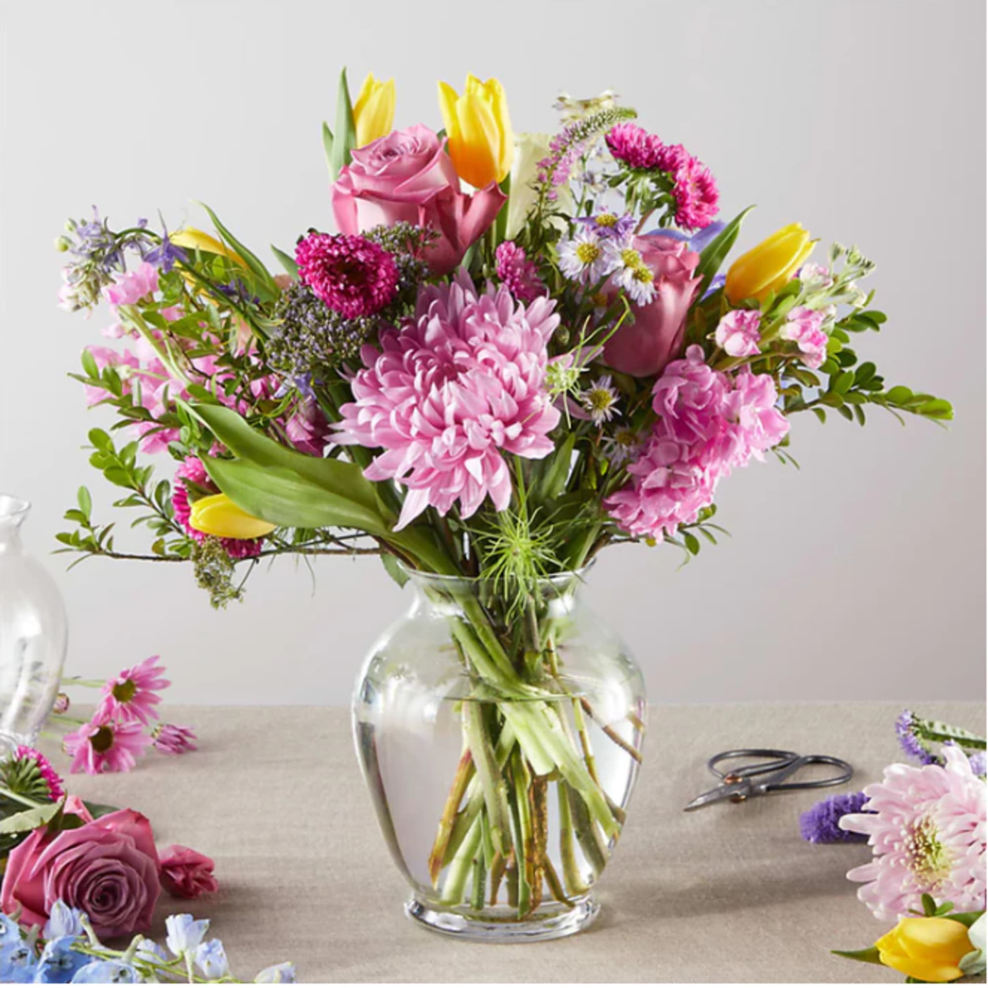 Mixed pink and yellow flowers arranged in a clear glass vase
