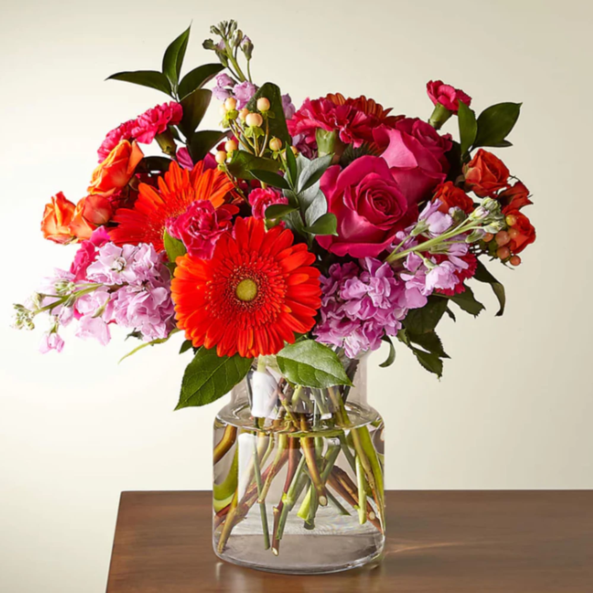 Bright mixed bouquet of roses, gerbera daisies, and pink blooms in a glass vase