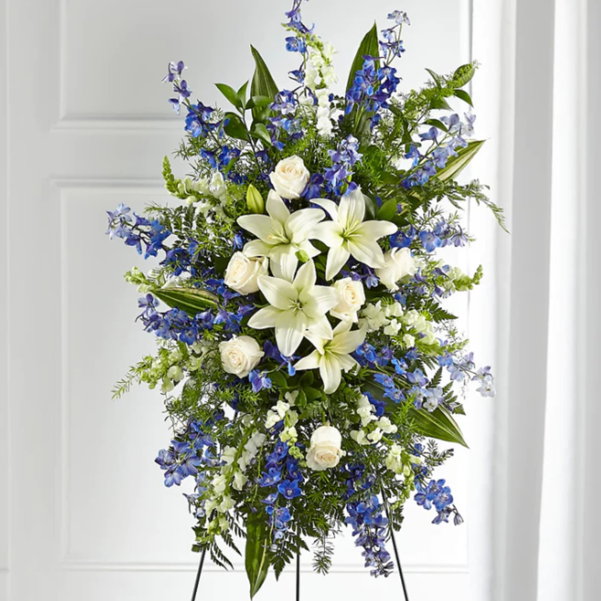 Tall standing spray of white lilies, white roses, and blue flowers