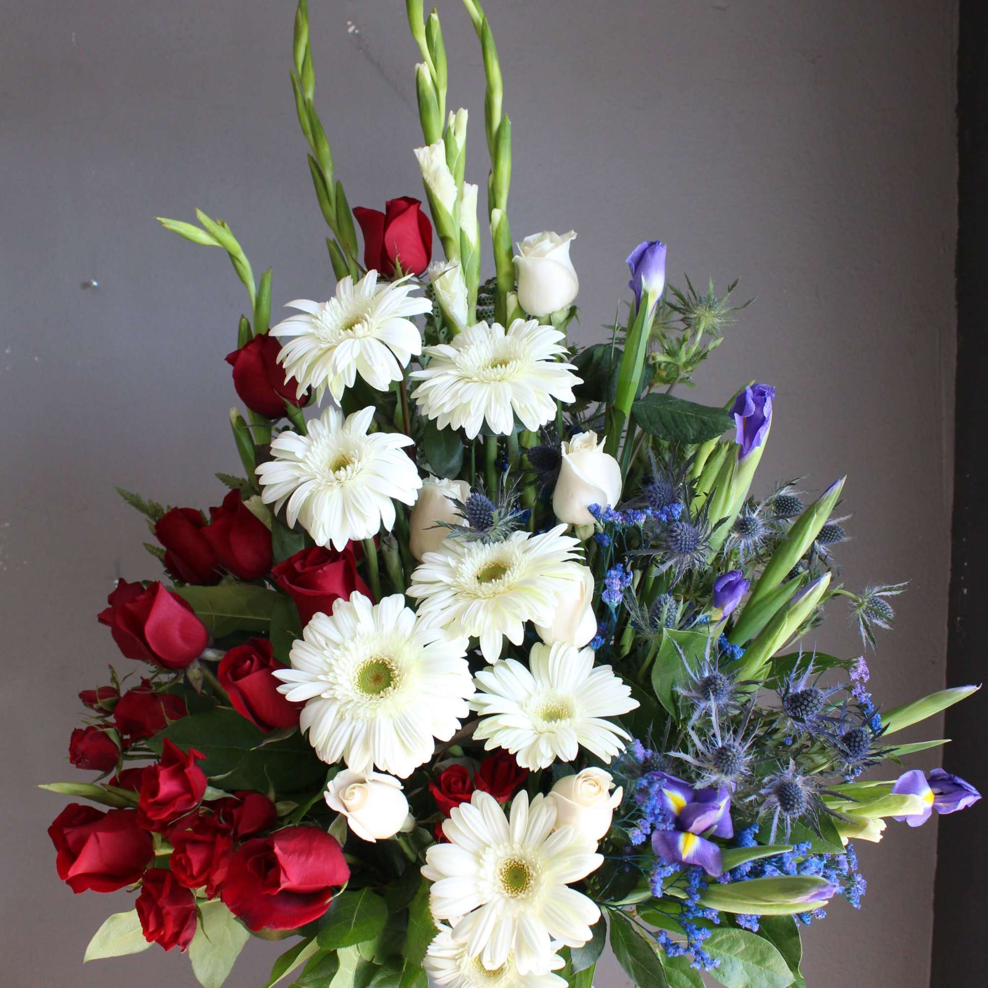 Tall bouquet of red roses, white daisies, and purple blooms in a white vase