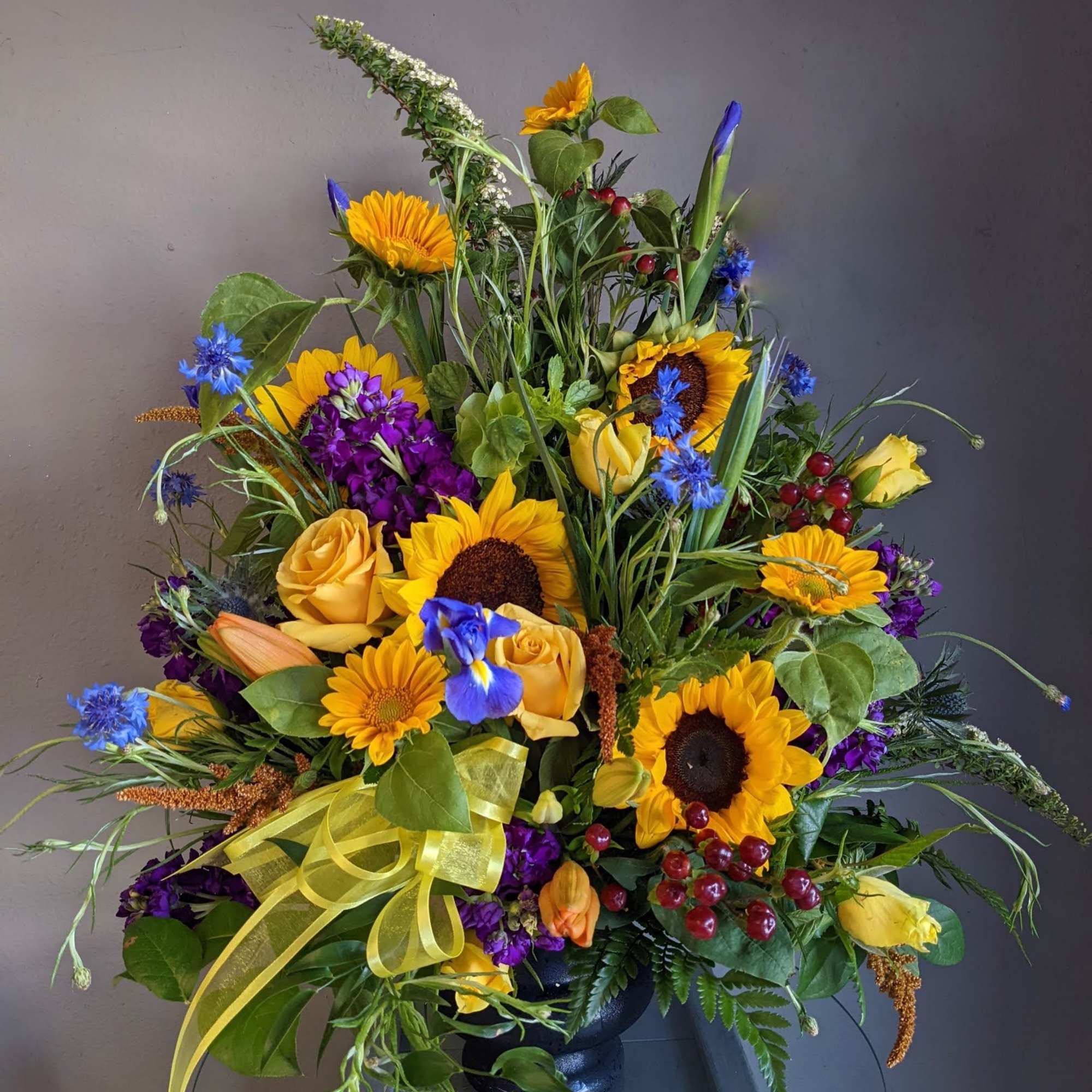 Large mixed bouquet with sunflowers, yellow roses, and purple flowers in a black vase