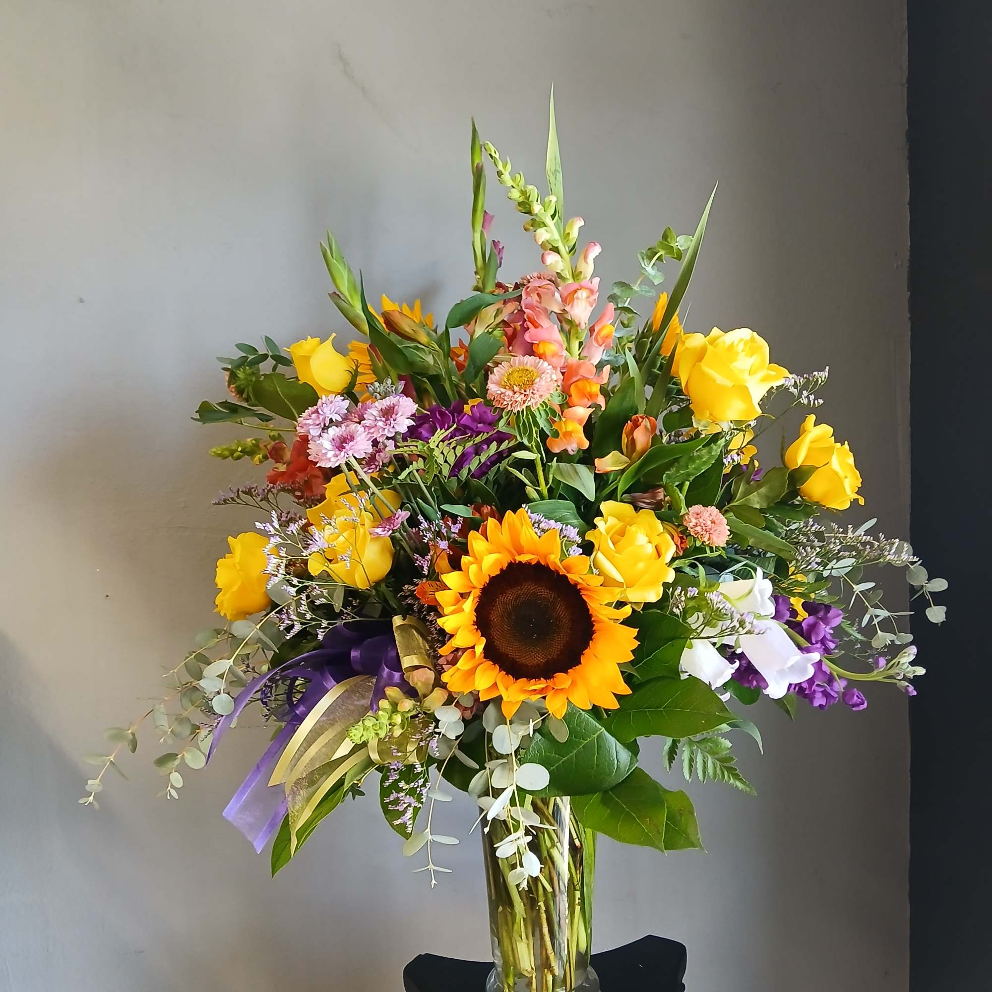 Mixed bouquet with sunflowers, yellow roses, and purple flowers in a glass vase