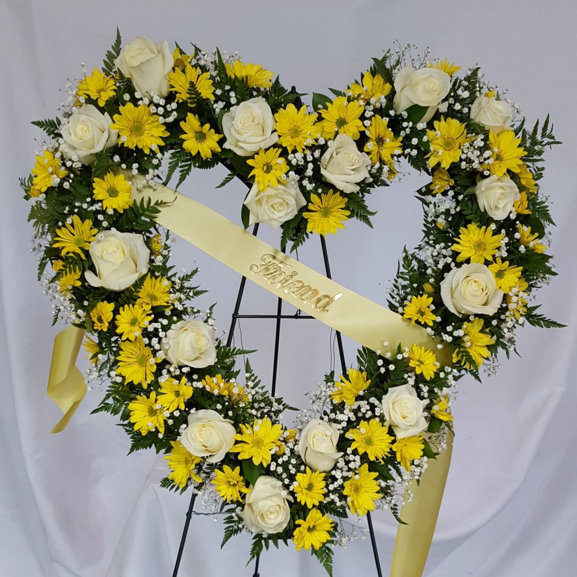 Heart-shaped floral wreath with white roses and yellow daisies on a stand