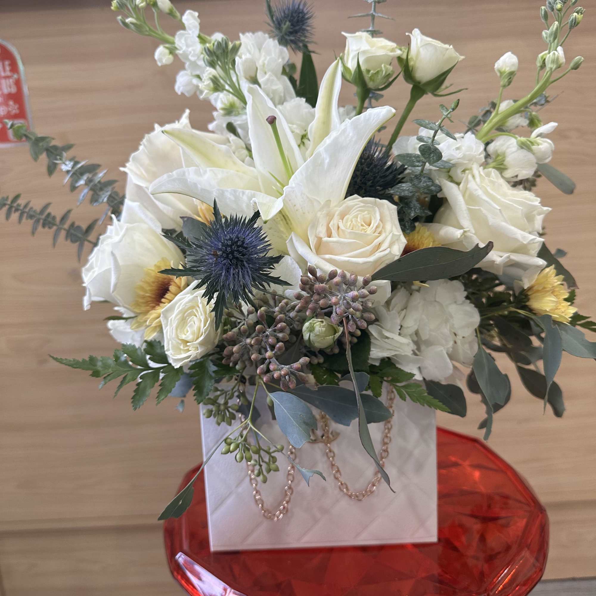 White bouquet with lilies, roses, and blue thistle in a white box