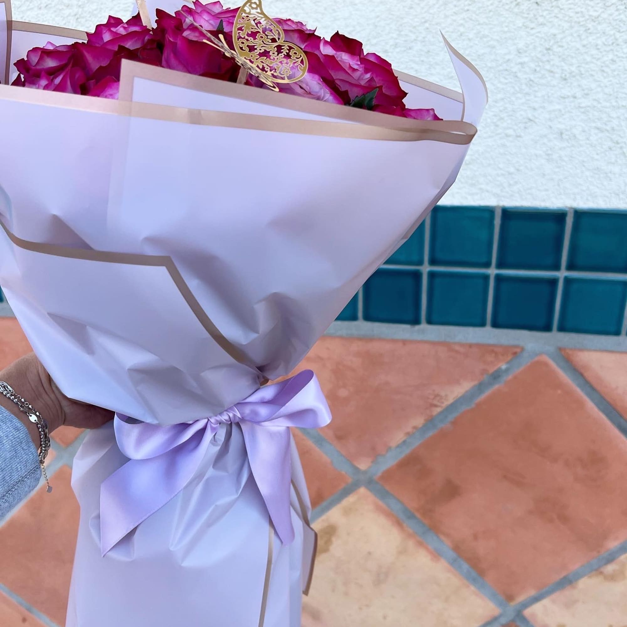 Bouquet of magenta roses wrapped in white paper with a lavender ribbon