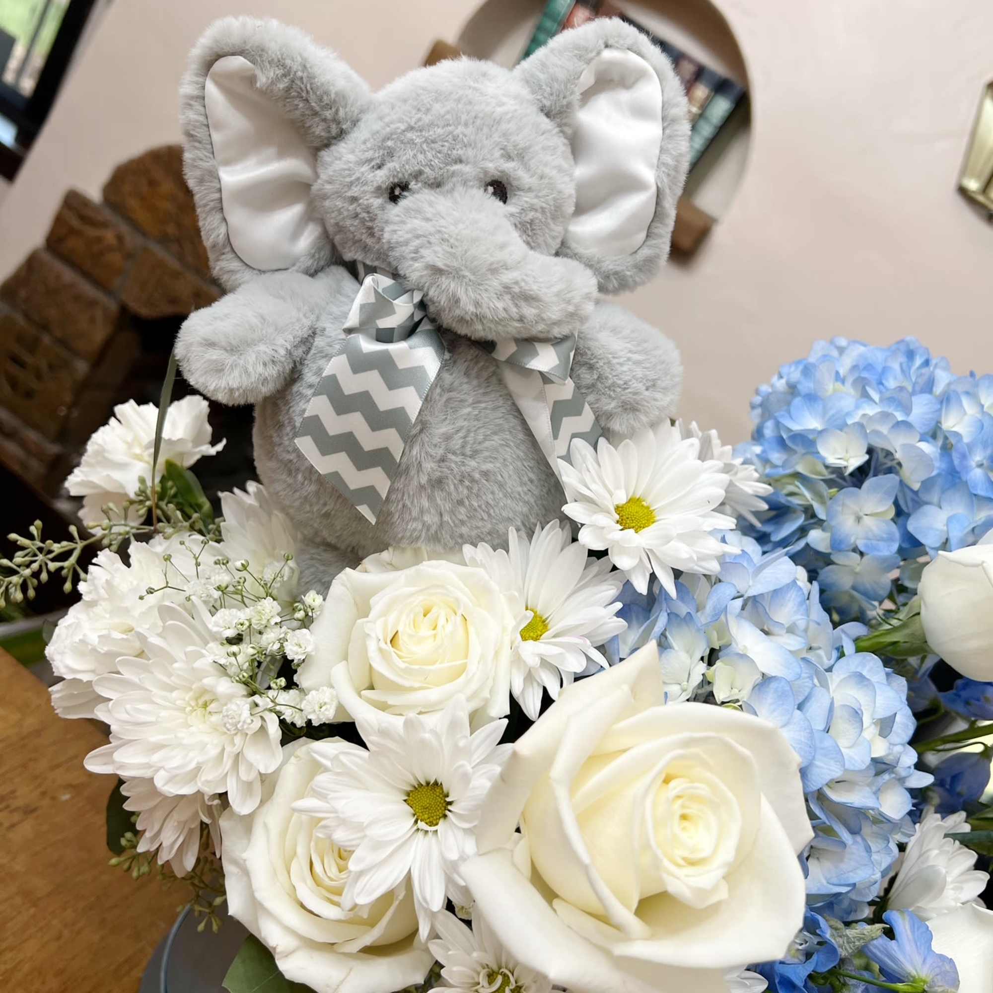 A white and blue floral arrangement, topped with a baby elephant, to