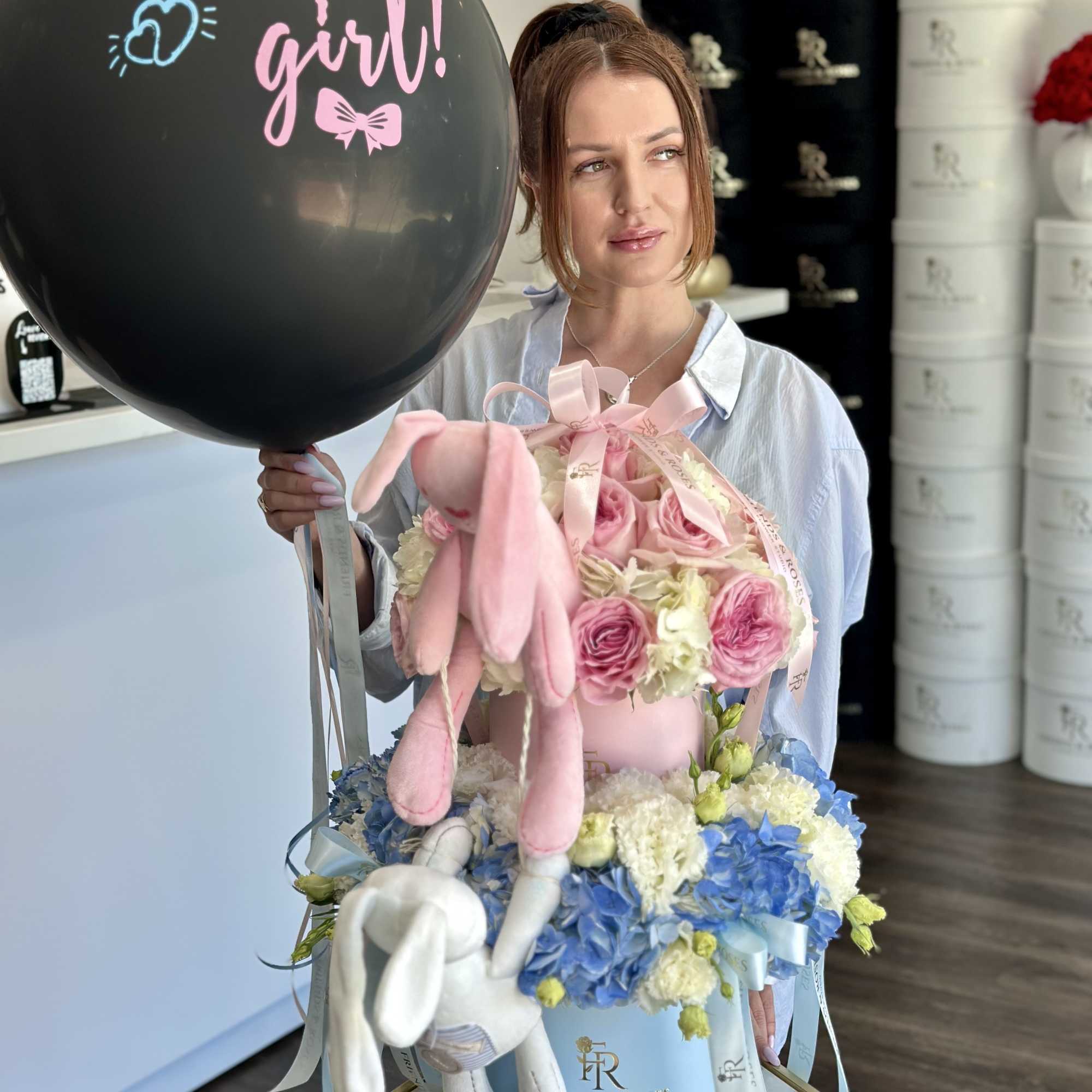 Woman holding a black balloon and a pastel flower box with plush bunnies